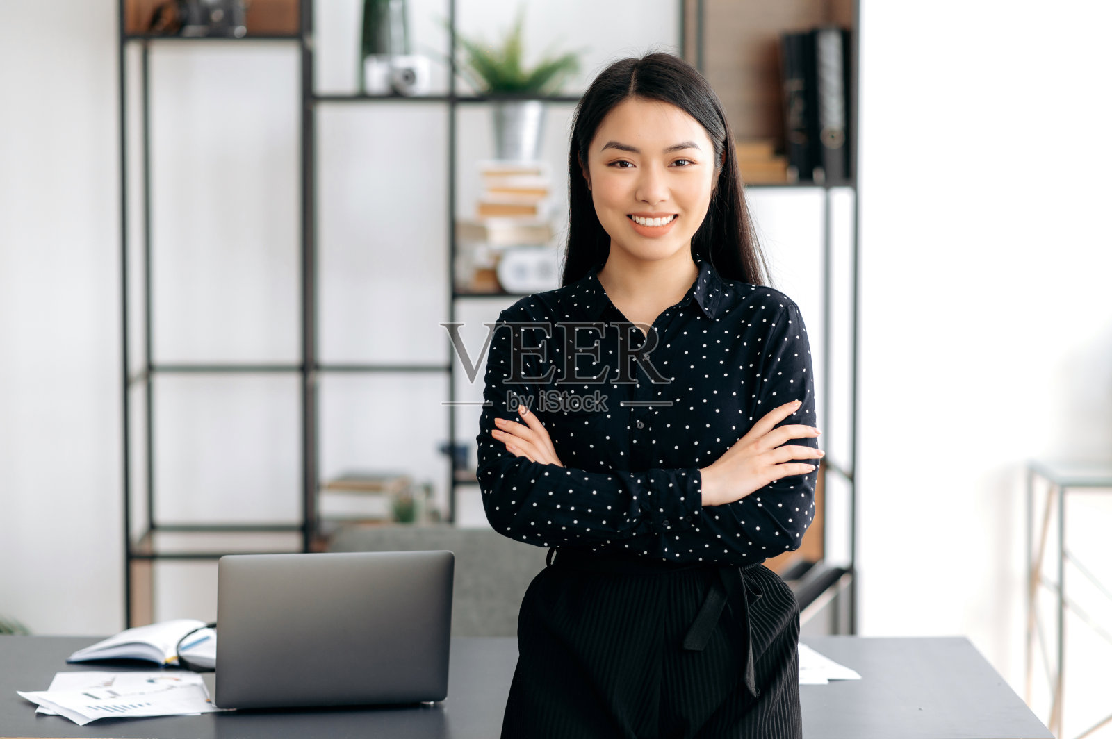 成功自信漂亮，年轻的亚洲女商人或自由职业者的肖像站在办公室的办公桌附近，穿着正式时尚的衣服，双臂交叉，看着相机，友好的微笑照片摄影图片