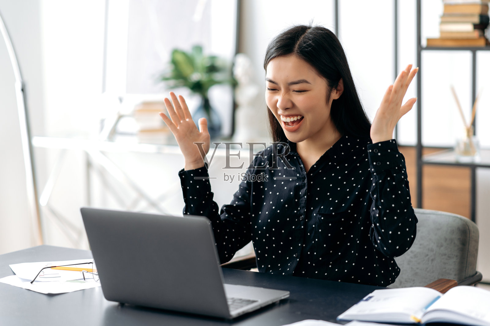 快乐幸运成功的亚洲年轻女性，时尚着装，办公室职员，自由职业者或学生坐在办公桌前，用她的手欢庆胜利，成功，好交易，大利润照片摄影图片