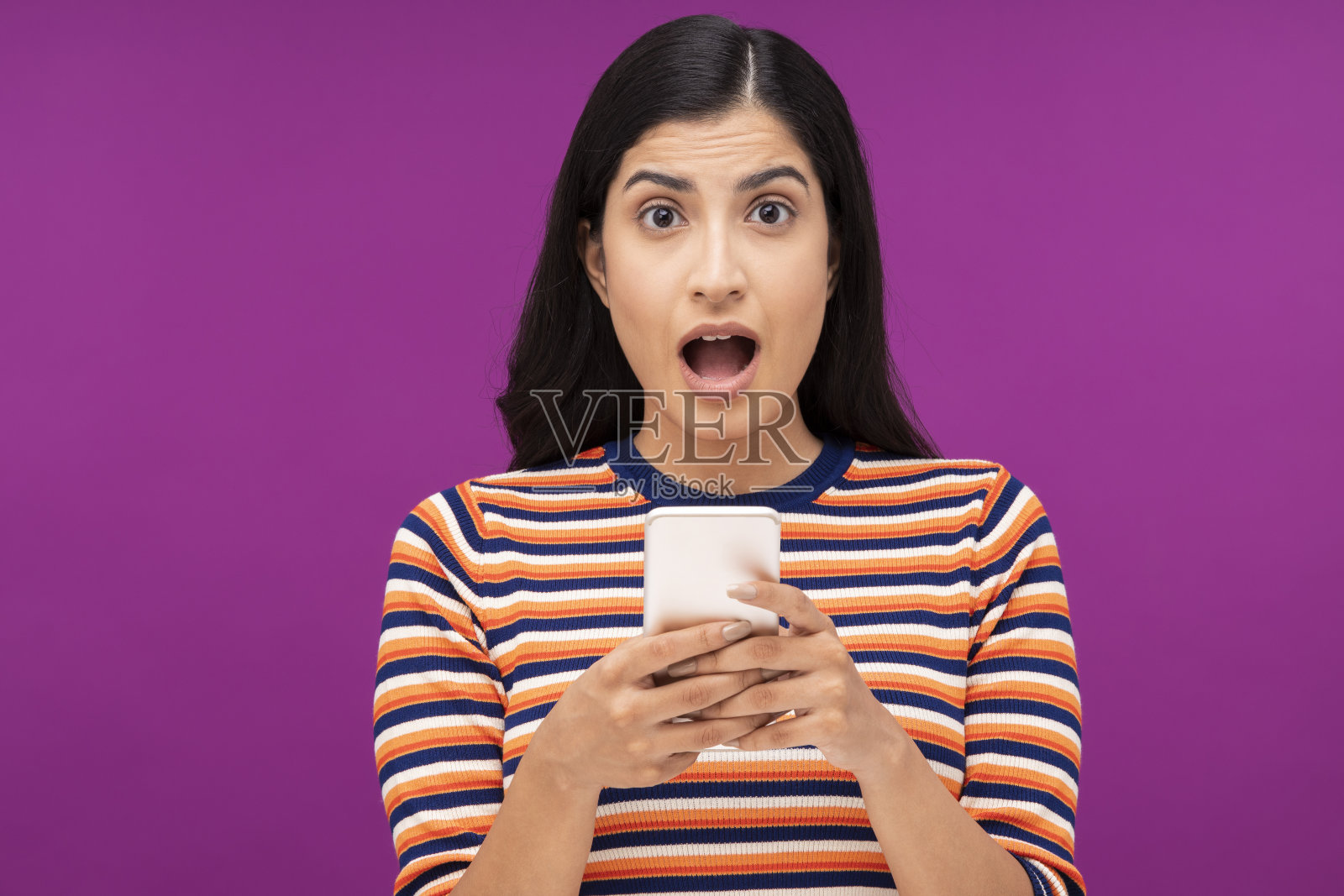 一名年轻女子的肖像，在紫色的背景下，孤立地站着，用手机在线聊天照片摄影图片