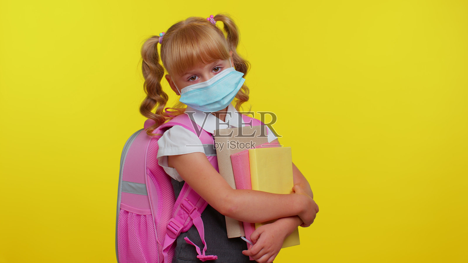 不健康的十几岁的女学生戴着保护性的医用口罩，站在书里看起来很累照片摄影图片