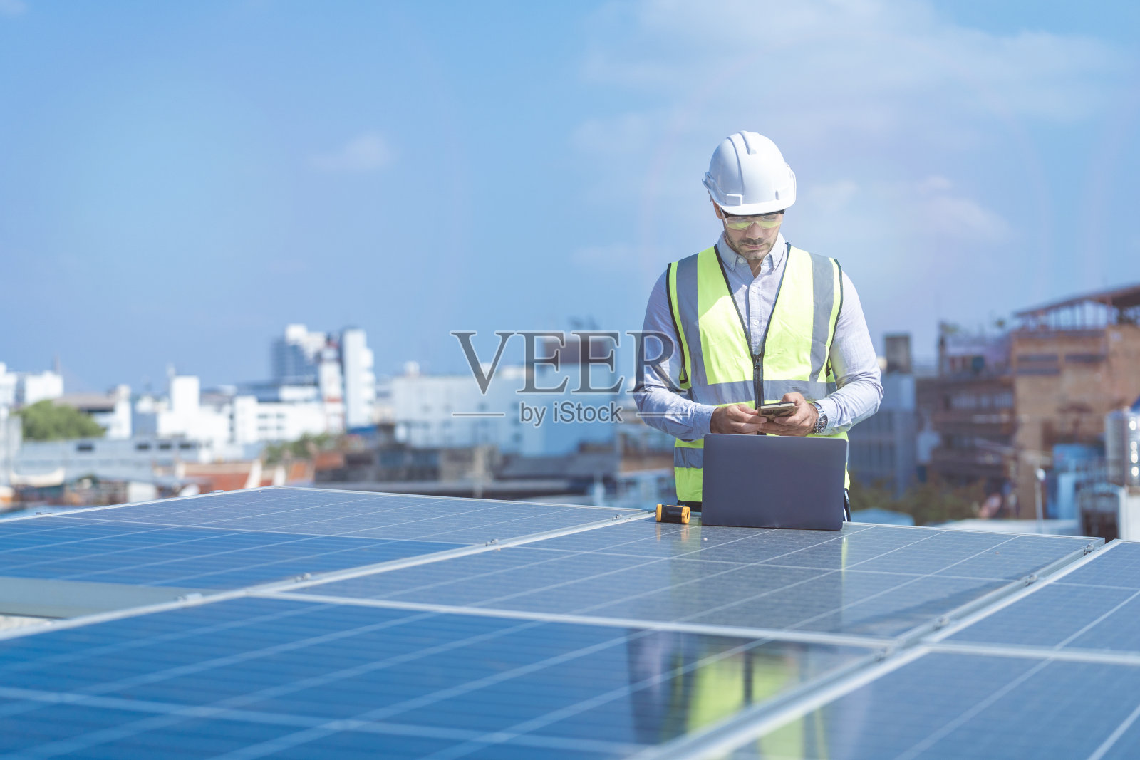 工程师通过笔记本电脑设备检查太阳能电池板或光伏电池的结构。绿色能源工业可再生能源。工厂工人在塔顶和摩天大楼城市工作。照片摄影图片
