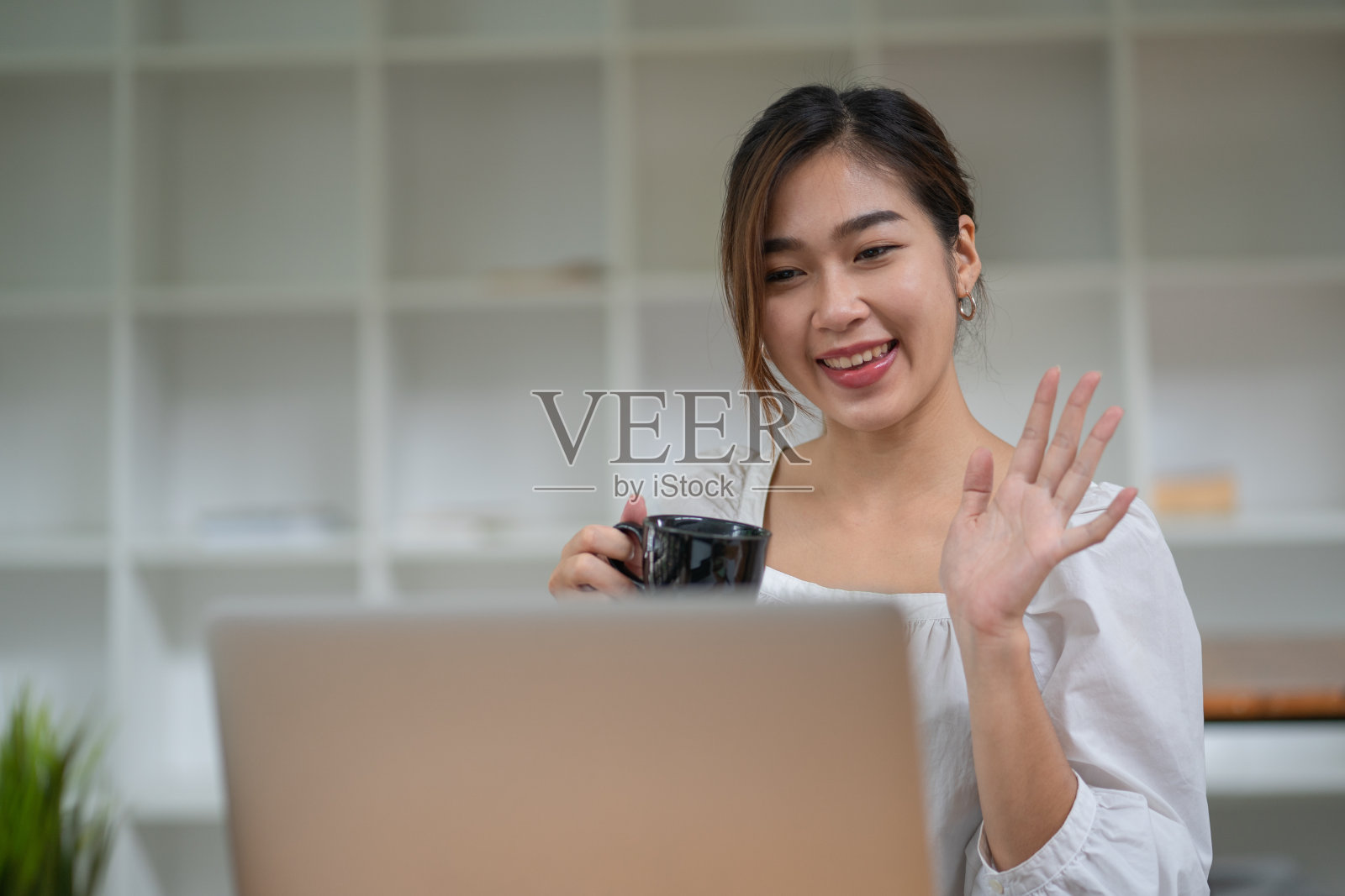 美丽的女商人拿着一杯咖啡放松与幸福的商业成功，而坐在她的办公桌办公室。照片摄影图片