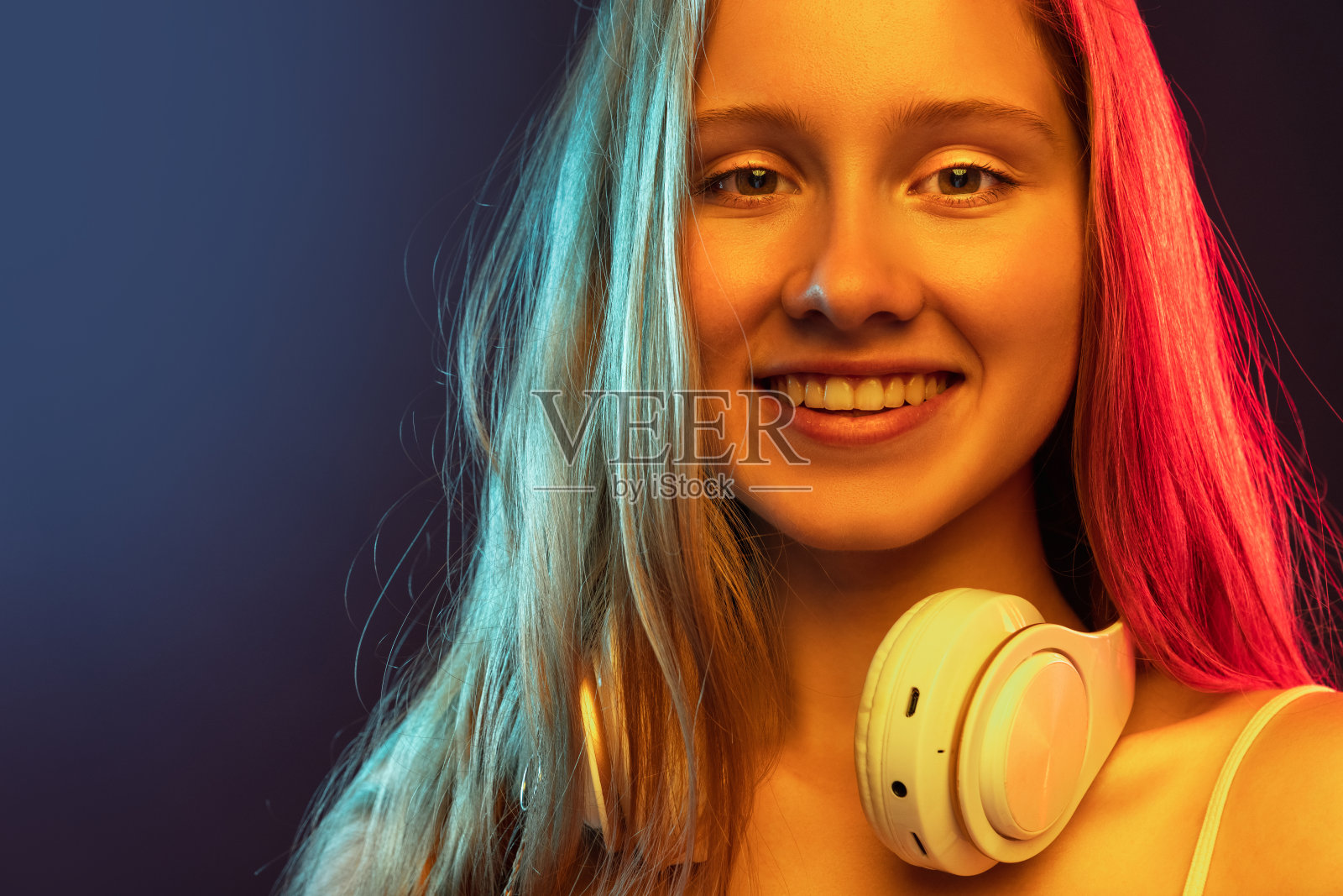 特写年轻微笑的女孩孤立在深蓝色的工作室背景在粉红色的霓虹灯。人类情感概念，面部表情，青春，销售，广告。照片摄影图片