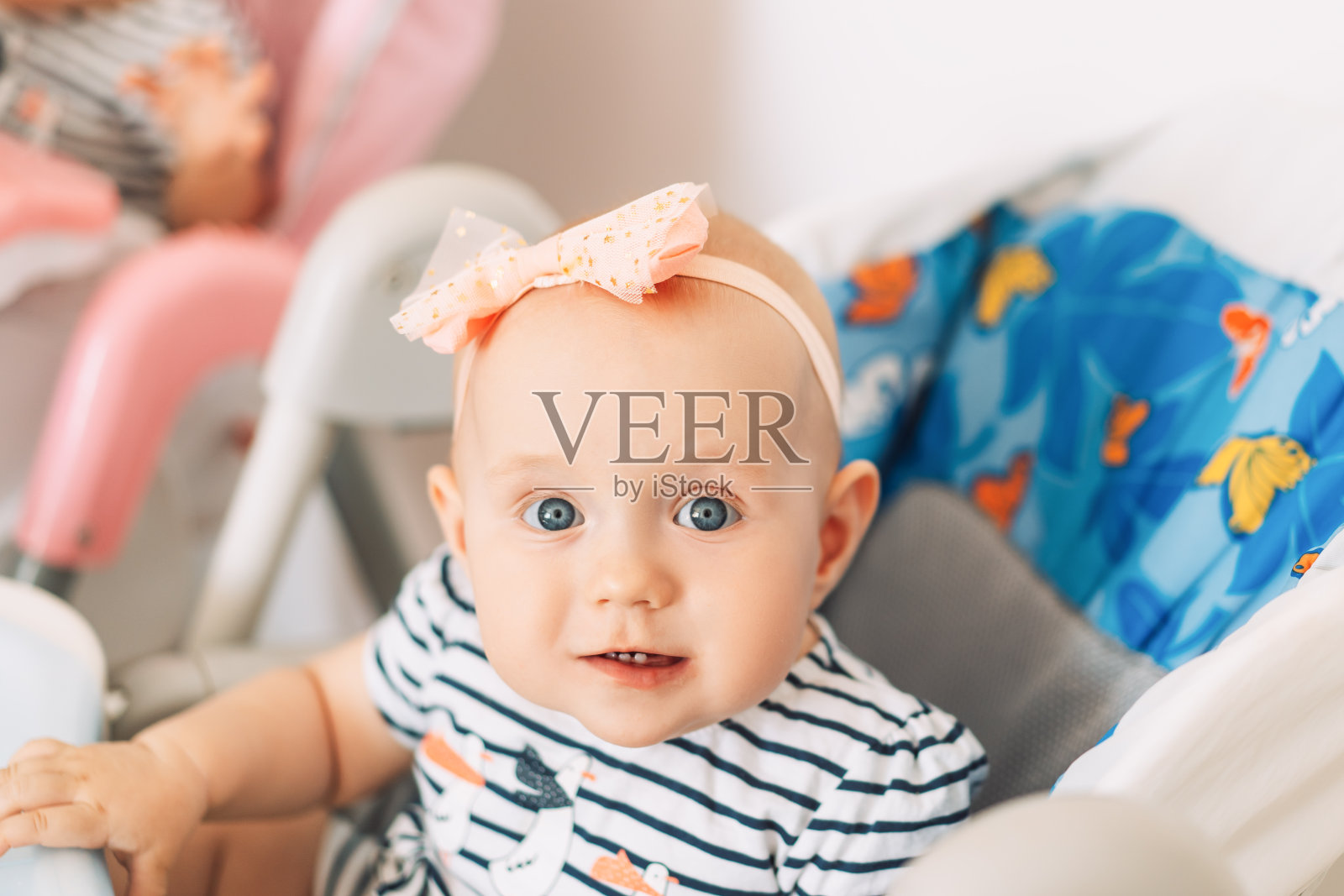 孩子坐在儿童座椅上，蓝眼睛，头上戴着蝴蝶结照片摄影图片