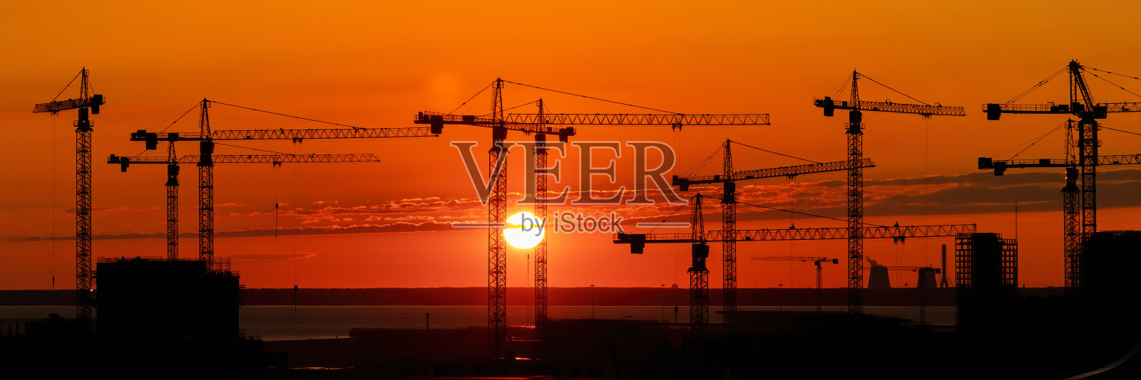 宽阔的工业景观全景上，许多建筑塔吊在火红和橘红色的夕阳映衬下。照片摄影图片