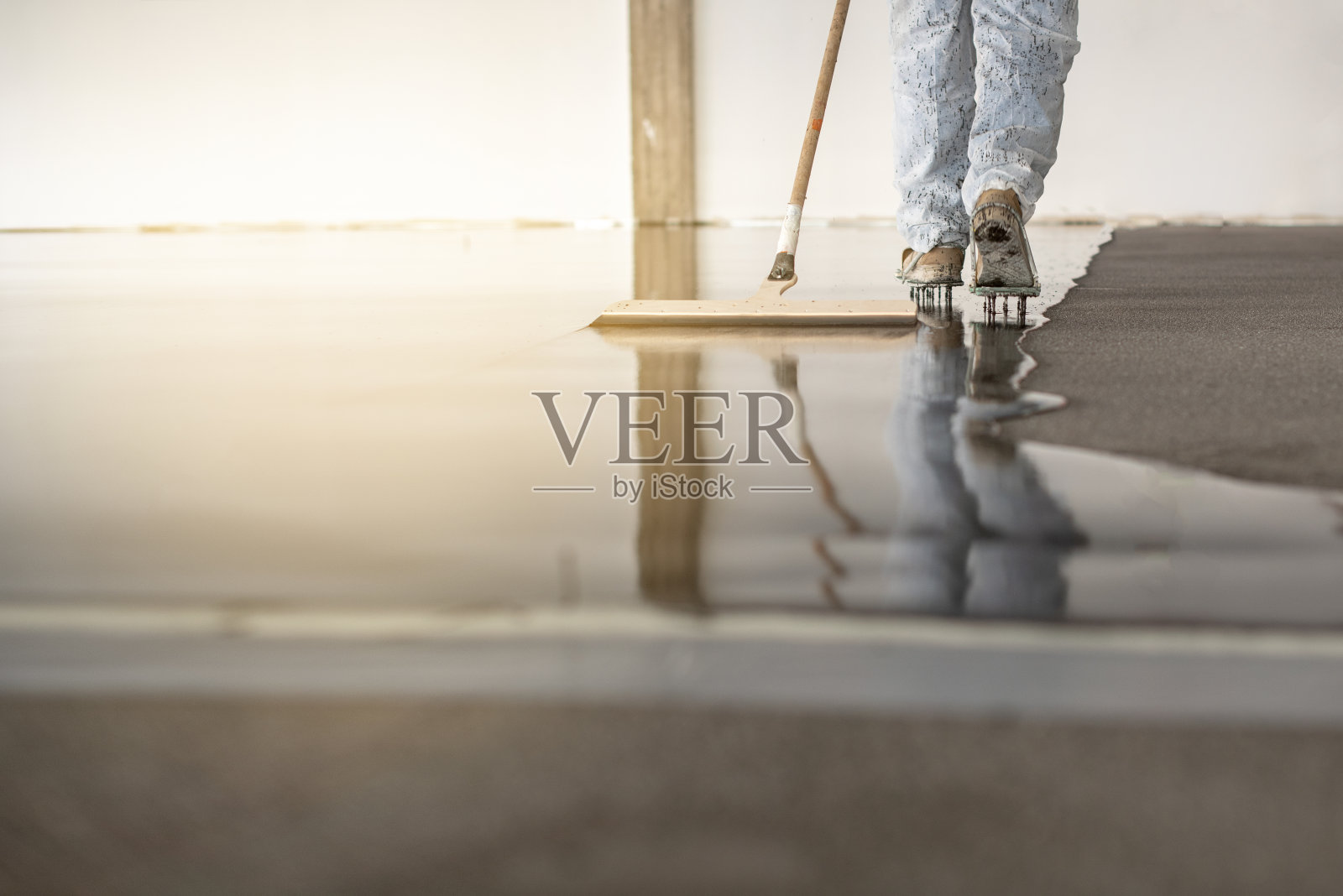 在工业大楼地板上工作的工人。施工人员正在灌浆和整理未干的混凝土地面。照片摄影图片