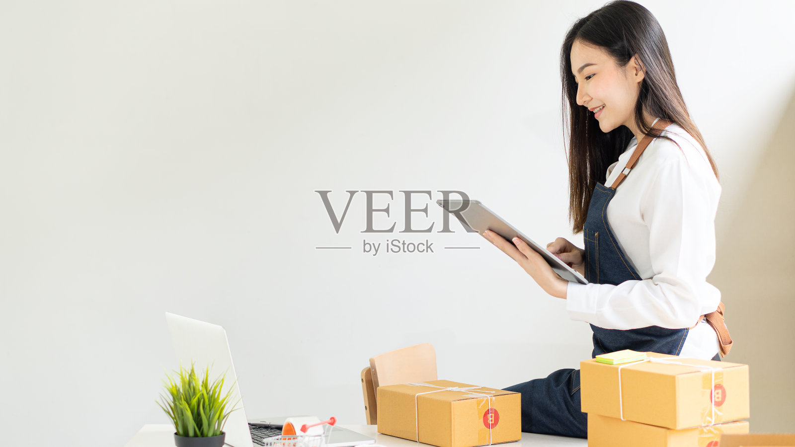 创业公司，小型企业，中小企业，亚洲女性企业家与盒子。微笑并用电脑检查销售赤字。之后，她成功地在网上中小企业业务上进行了不同的思考。照片摄影图片