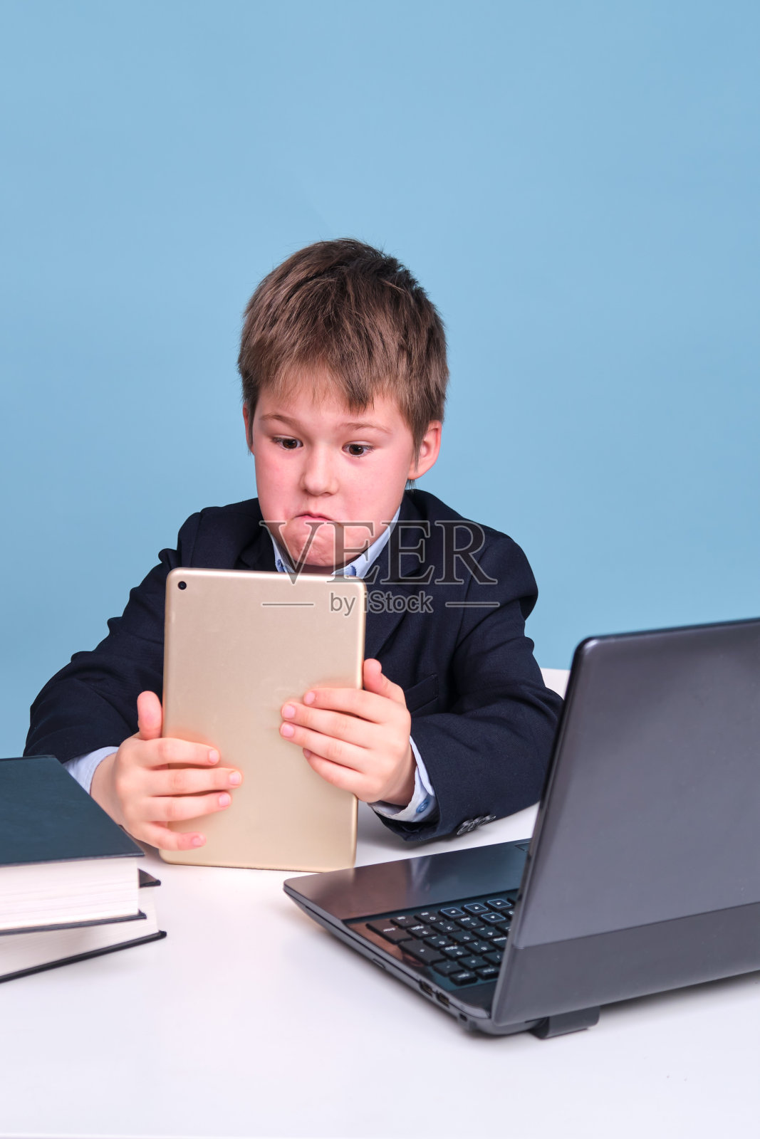 一个男孩穿着校服，手里拿着一个远程学习的数字平板电脑，在蓝色的工作室背景上复制空间照片摄影图片