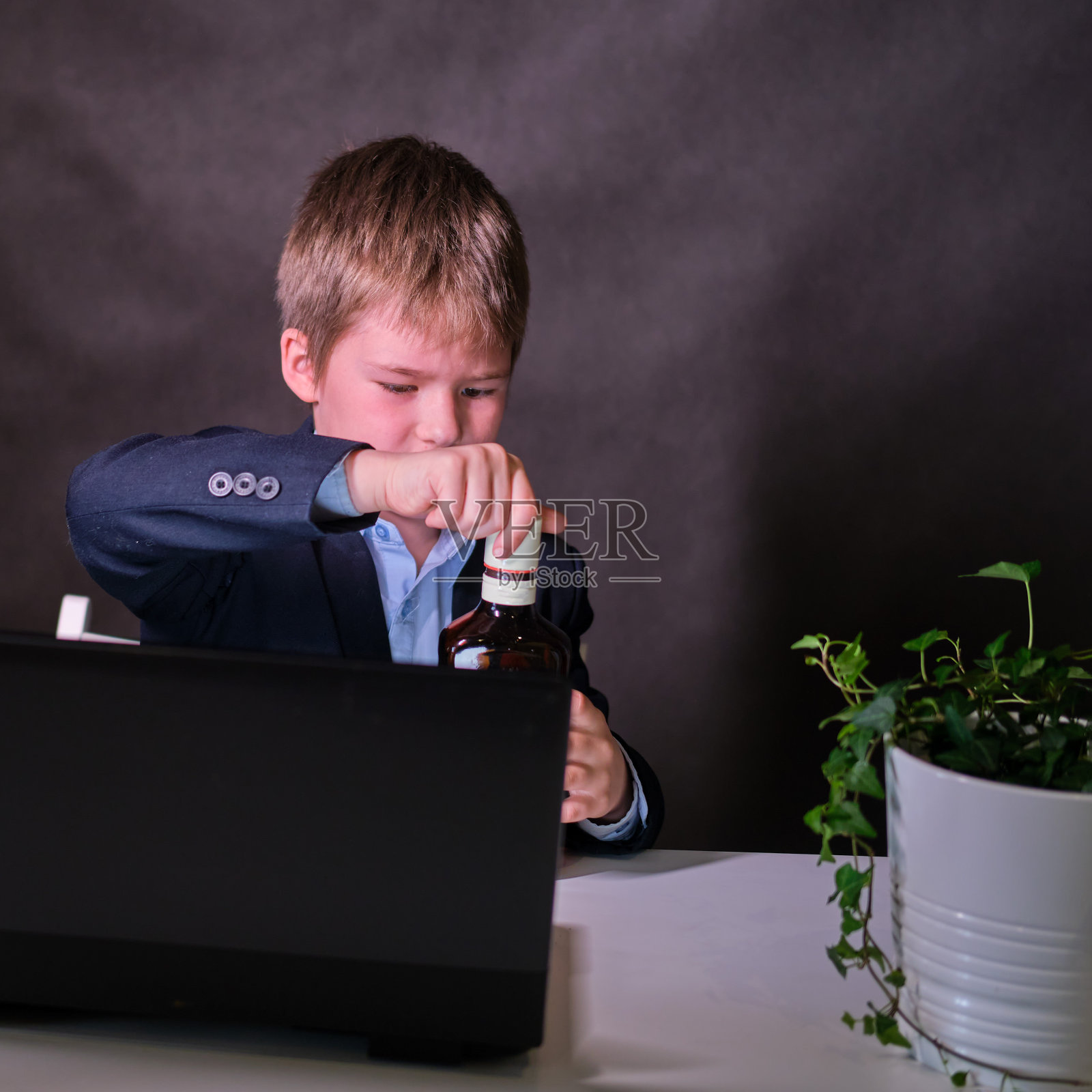 一个快乐的男孩穿着校服，手里拿着一瓶酒，在黑暗的工作室背景上复制空间照片摄影图片