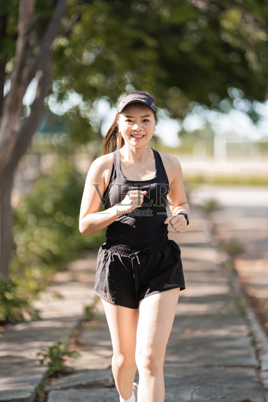 一位健康快乐的亚洲女性跑步者，身穿黑色运动服，在日落下在自然城市公园慢跑照片摄影图片