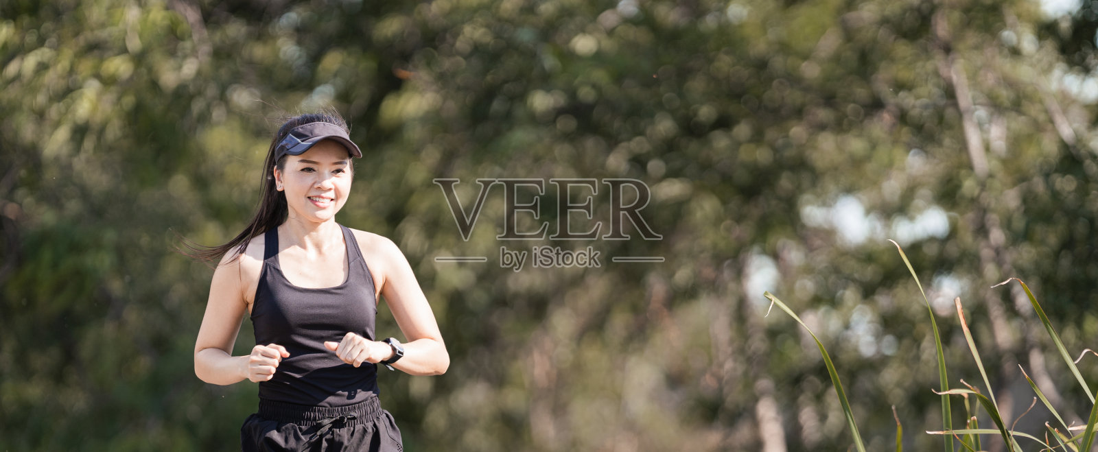 一位健康快乐的亚洲女性跑步者，身穿黑色运动服，在日落下在自然城市公园慢跑照片摄影图片