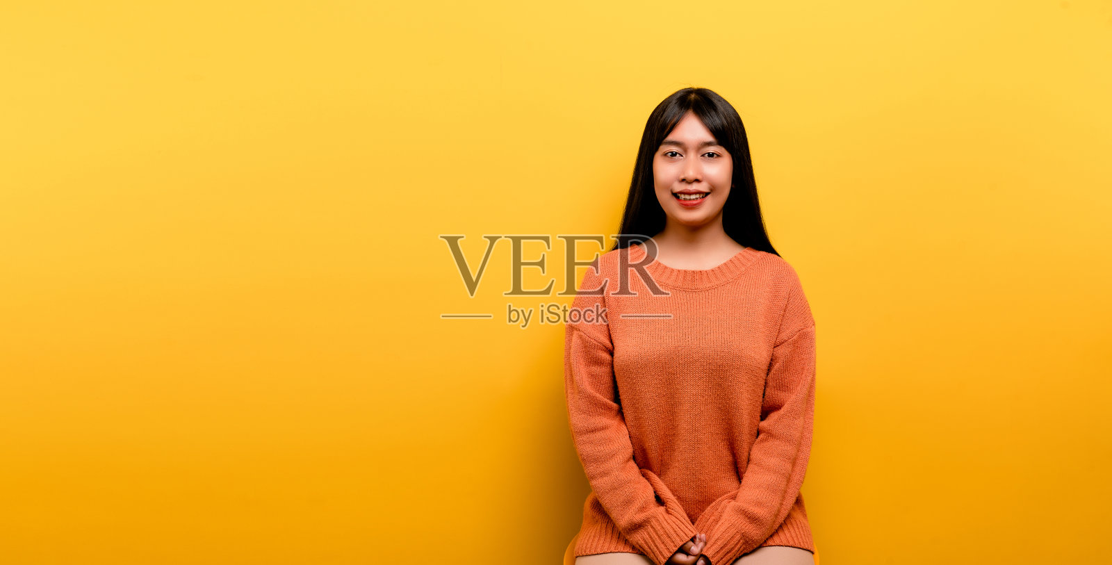 漂亮的亚洲女孩穿着一件橙色的休闲连衣裙。用快乐的微笑和胜利者的表情举手庆祝胜利。快乐的表情照片摄影图片