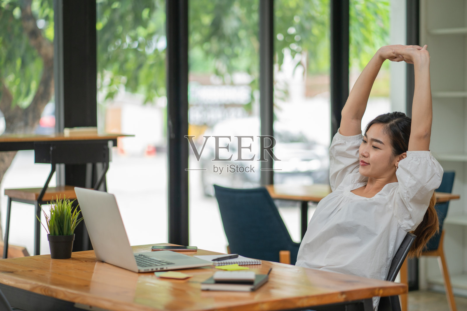 一个快乐放松的年轻女人坐在她的办公室里，面前放着一台笔记本电脑，双臂伸过头顶照片摄影图片