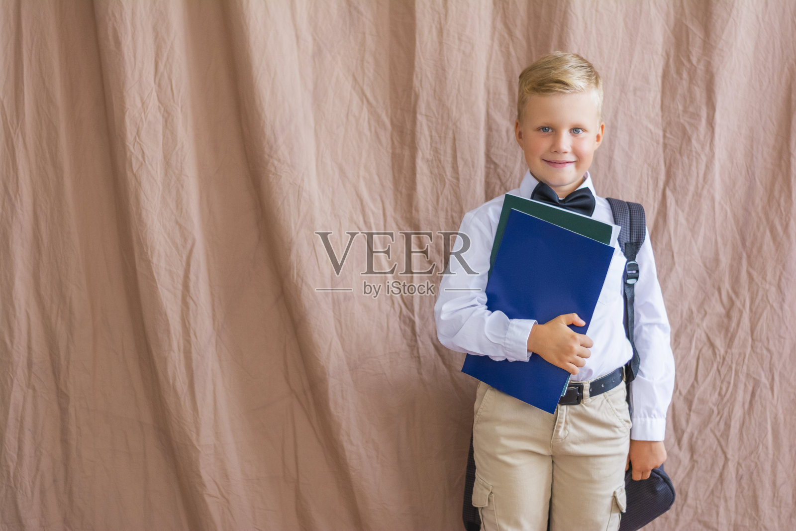 笑容满面的男学生拿着一本关于工作室背景的书回到学校。空的空间照片摄影图片