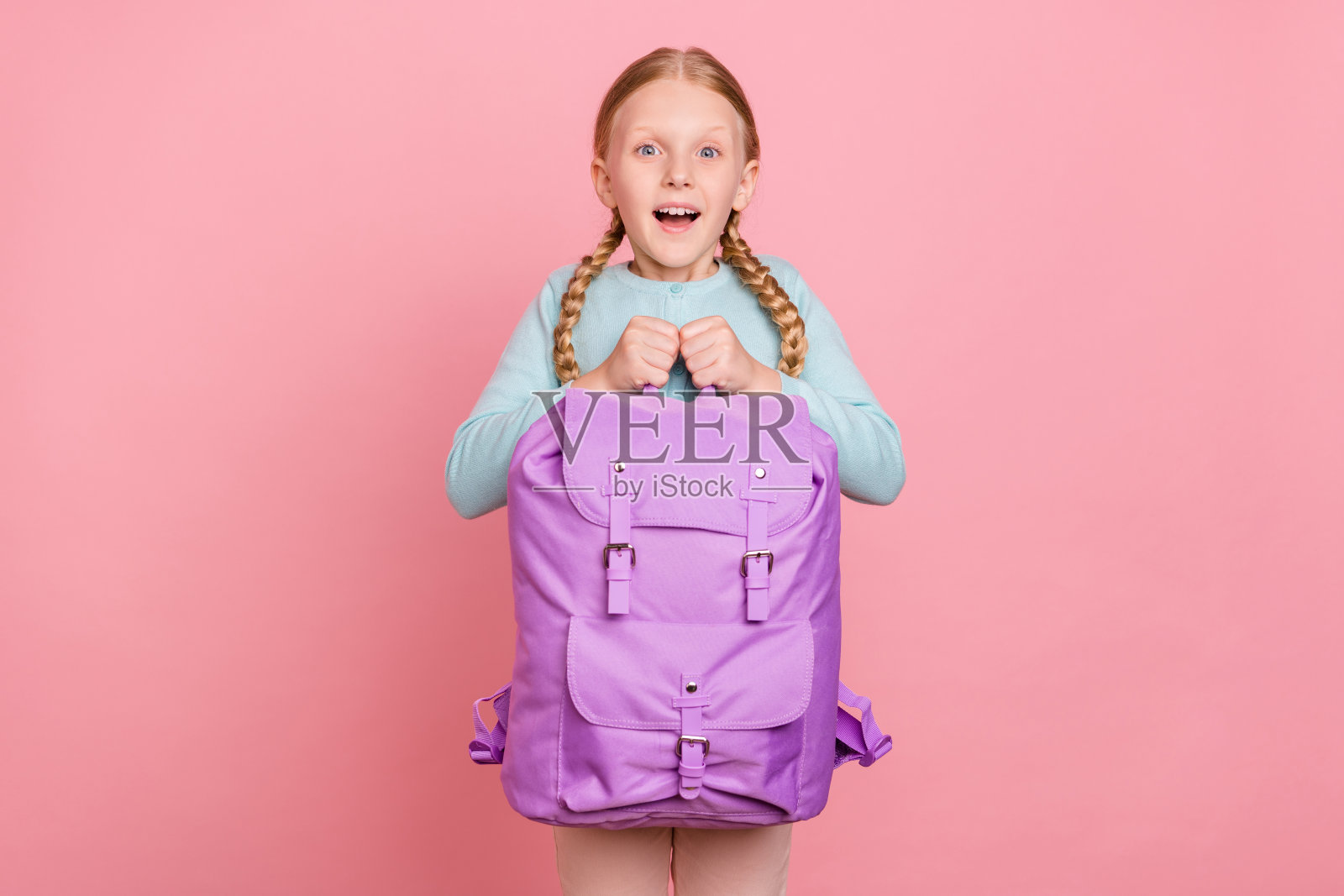 可爱的震惊女学生穿着蓝色开衫微笑着拿着背包孤立的粉红色背景照片摄影图片