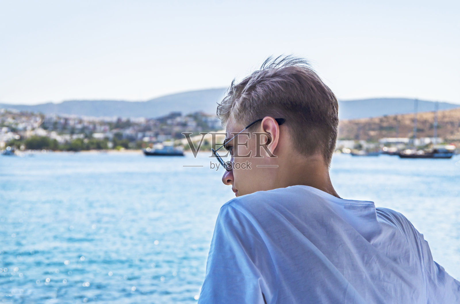 一个年轻人，15-18岁的少年，戴着太阳镜躺在沙滩上，享受着海水蓝色背景下的风景照片摄影图片