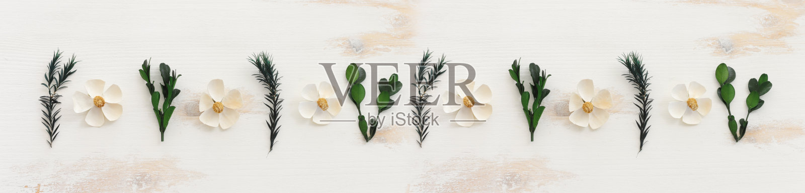 在木制背景上的白色和绿色的花组成的俯视图图像。平铺照片摄影图片