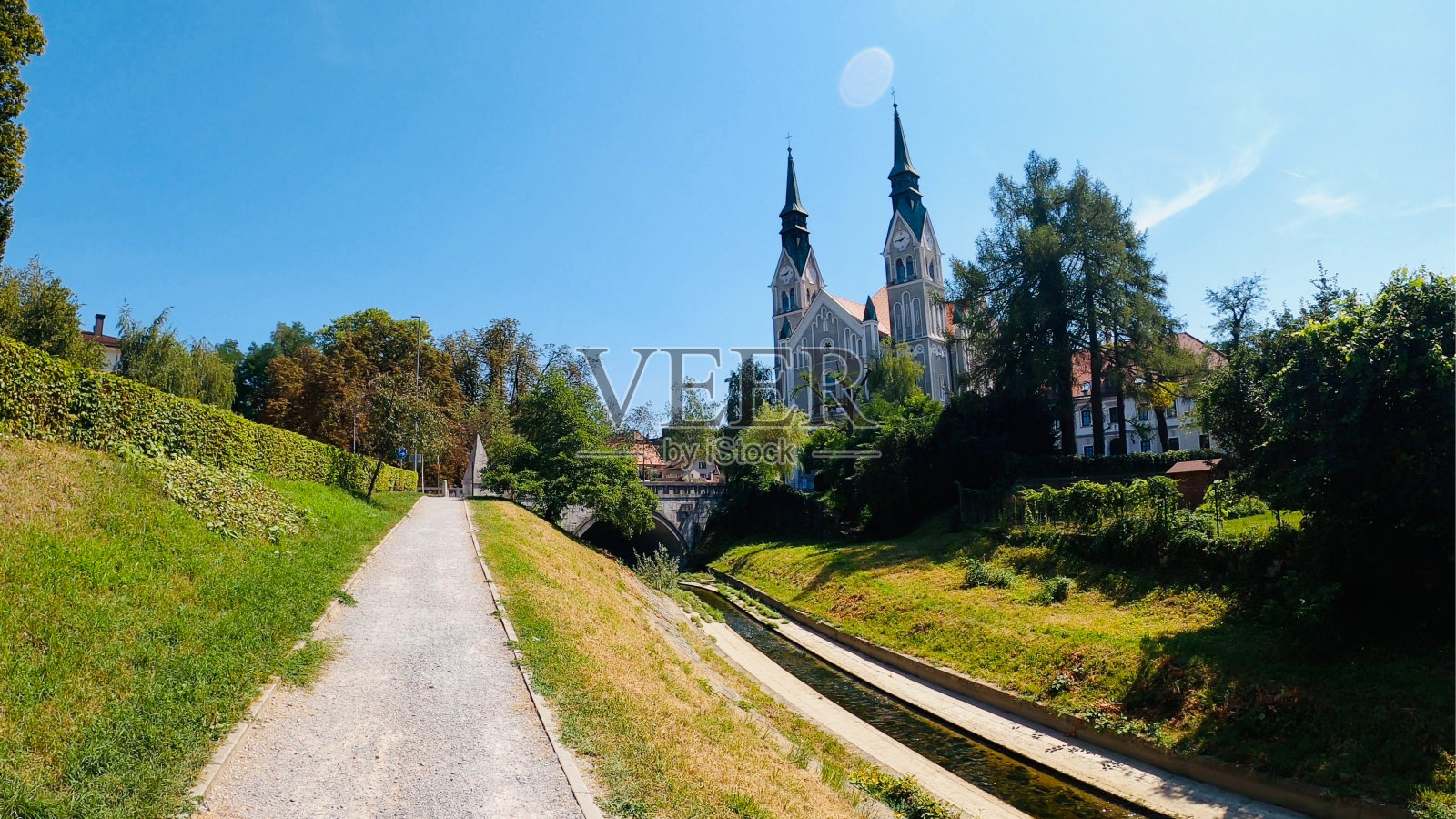在卢布尔雅那的城市花园中放松的夏日漫步，附近有一条小河，背景中有一座教堂和一座桥。照片摄影图片
