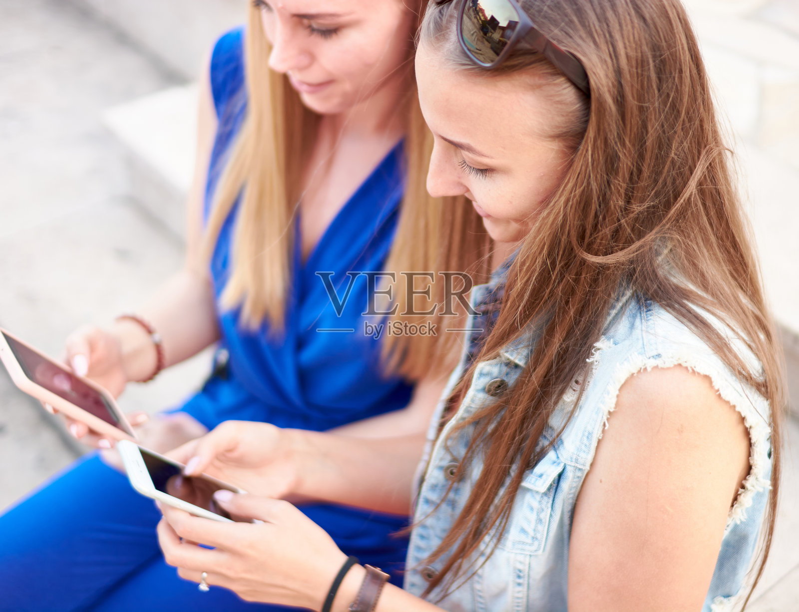 微笑着，年轻的千禧一代女性朋友们在智能手机上查看社交媒体更新——两个快乐的女人坐在长凳上，从网店订购鞋子——购物狂网红概念照片摄影图片