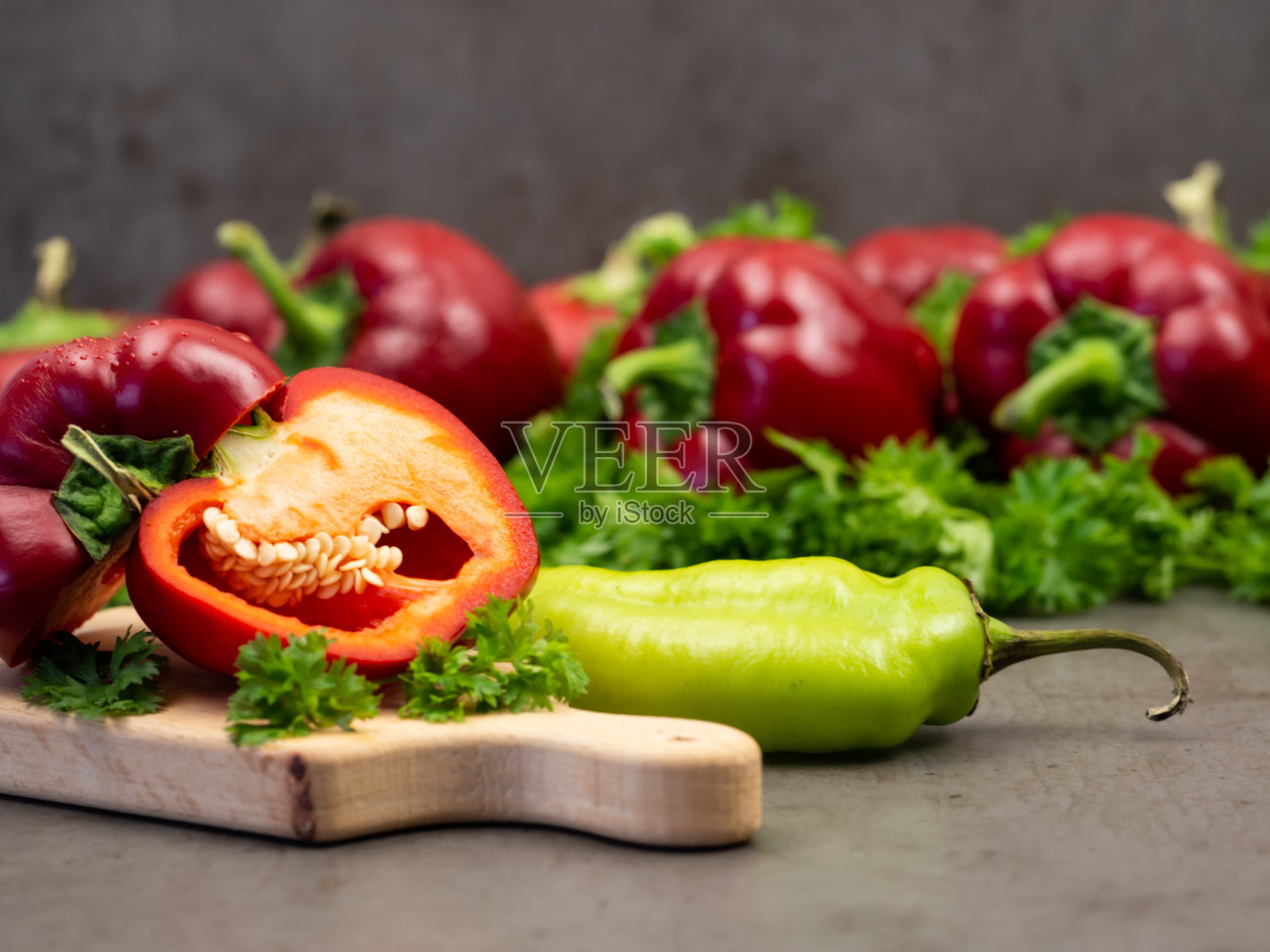 红甜椒，切成两半，欧芹放在木板上。灰色的背景。蔬菜。照片摄影图片