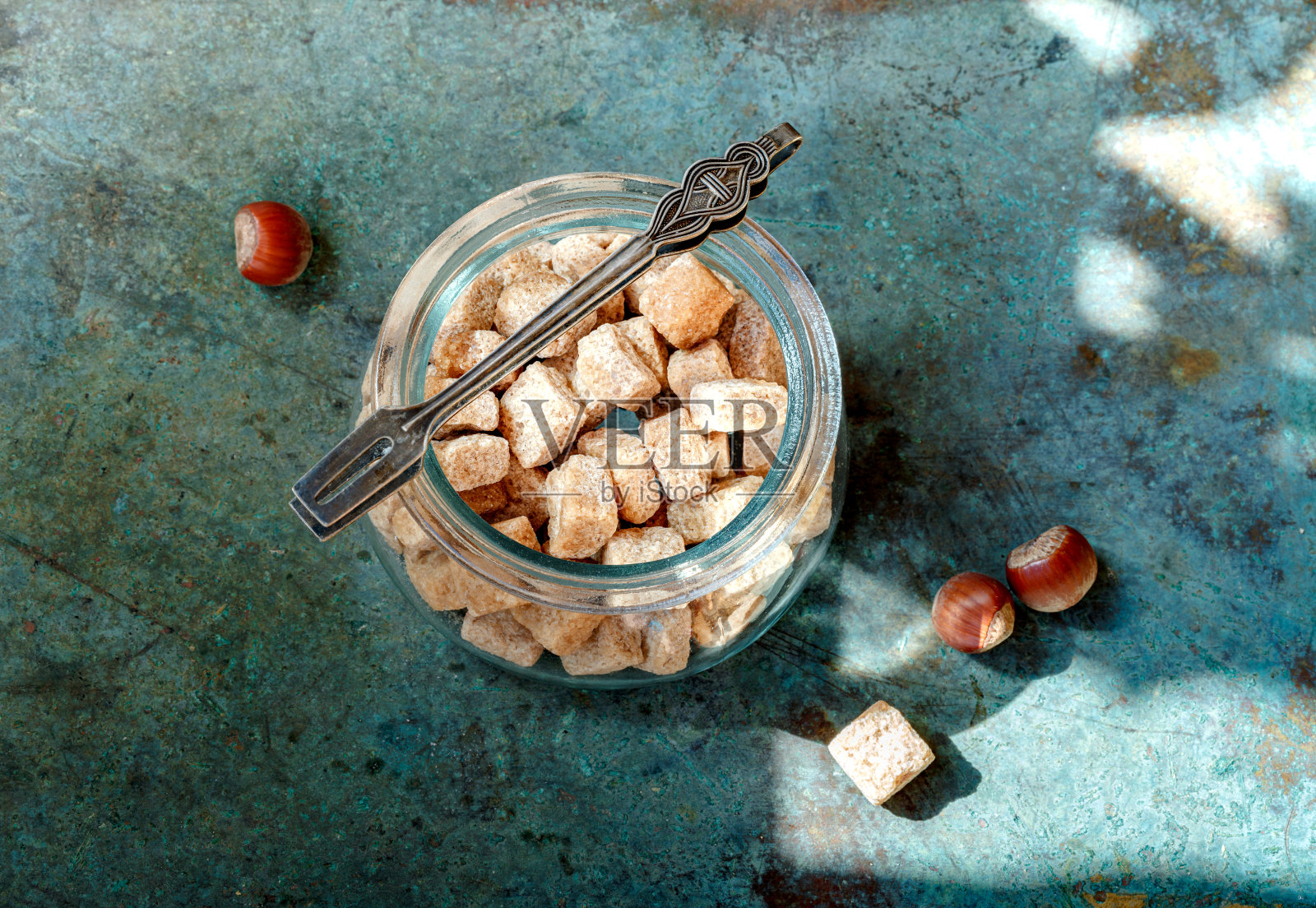 一碗带糖钳的甘蔗方糖和栗子放在蓝色的复古背景上。照片摄影图片