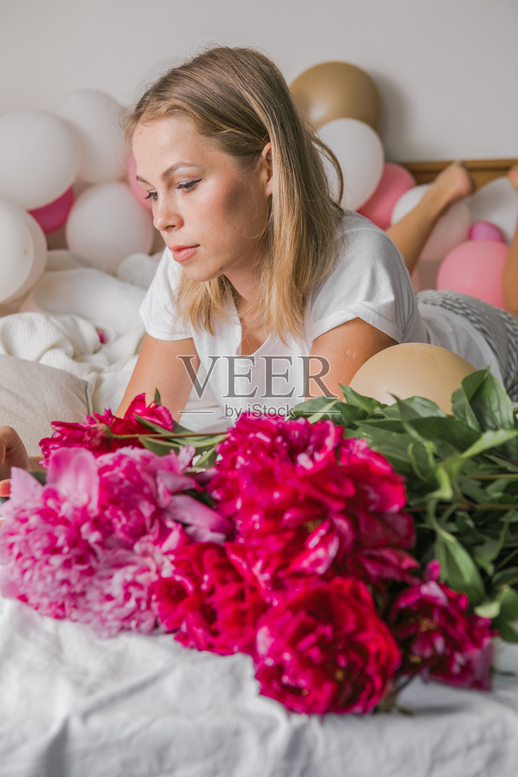 在线约会概念，在线社交概念。一个快乐积极的年轻漂亮女人在室内，在家，在卧室，在床上，拿着花，用手机自拍。照片摄影图片