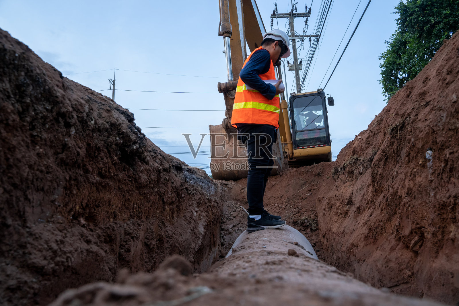 施工现场工程师穿着安全制服检查开挖混凝土排水管。照片摄影图片