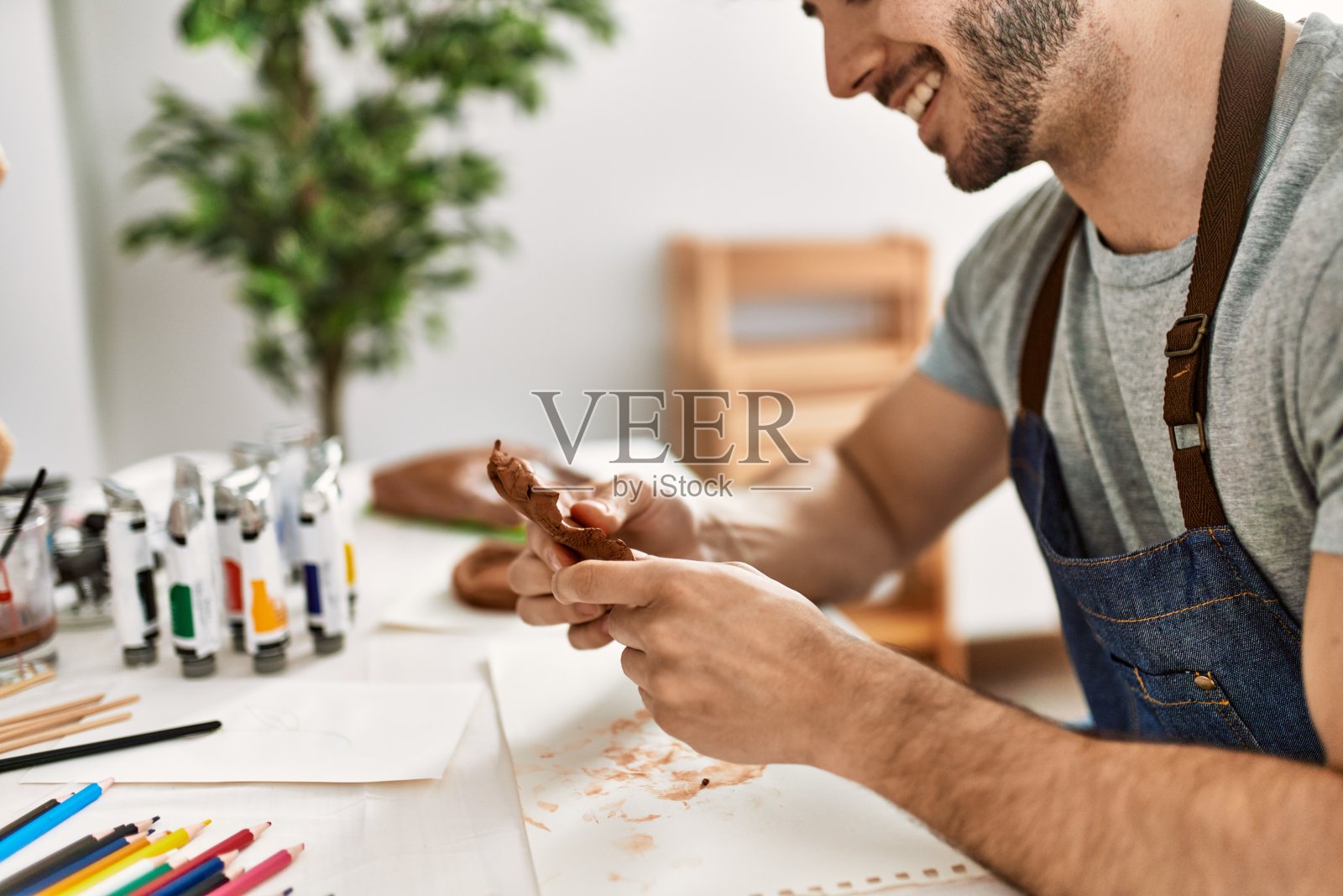 年轻的西班牙艺术家男人微笑快乐的造型在艺术工作室的陶器。照片摄影图片