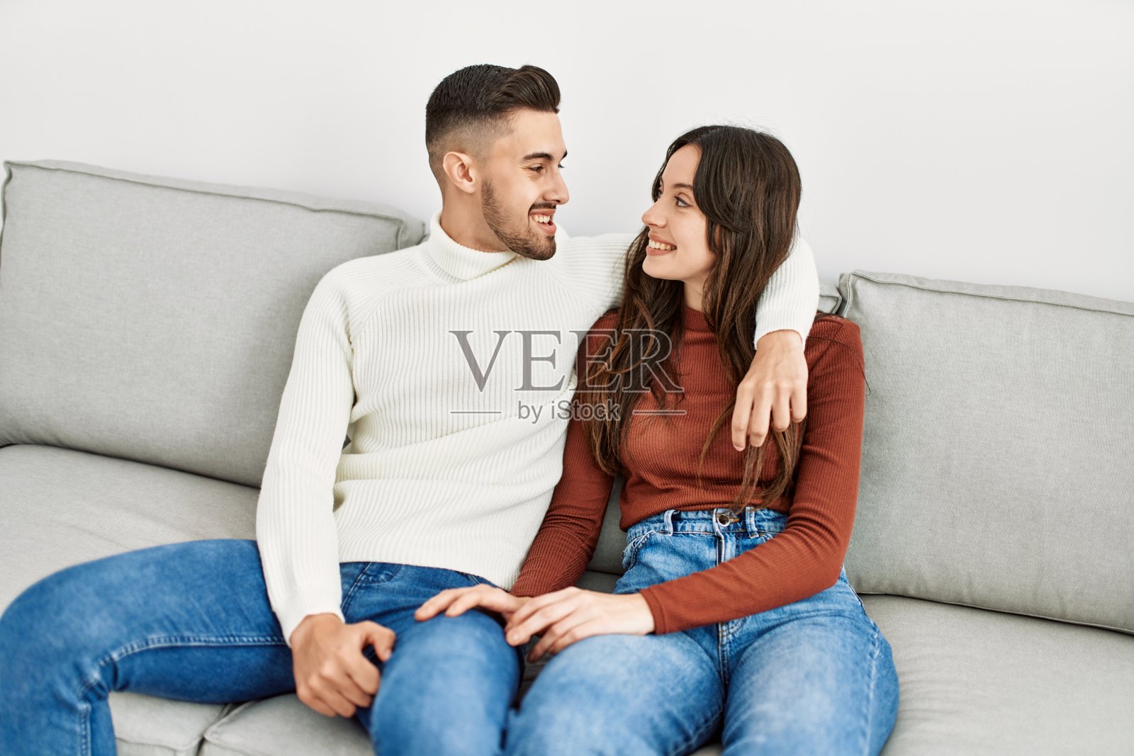 年轻的西班牙夫妇坐在沙发上，在家里拥抱。照片摄影图片