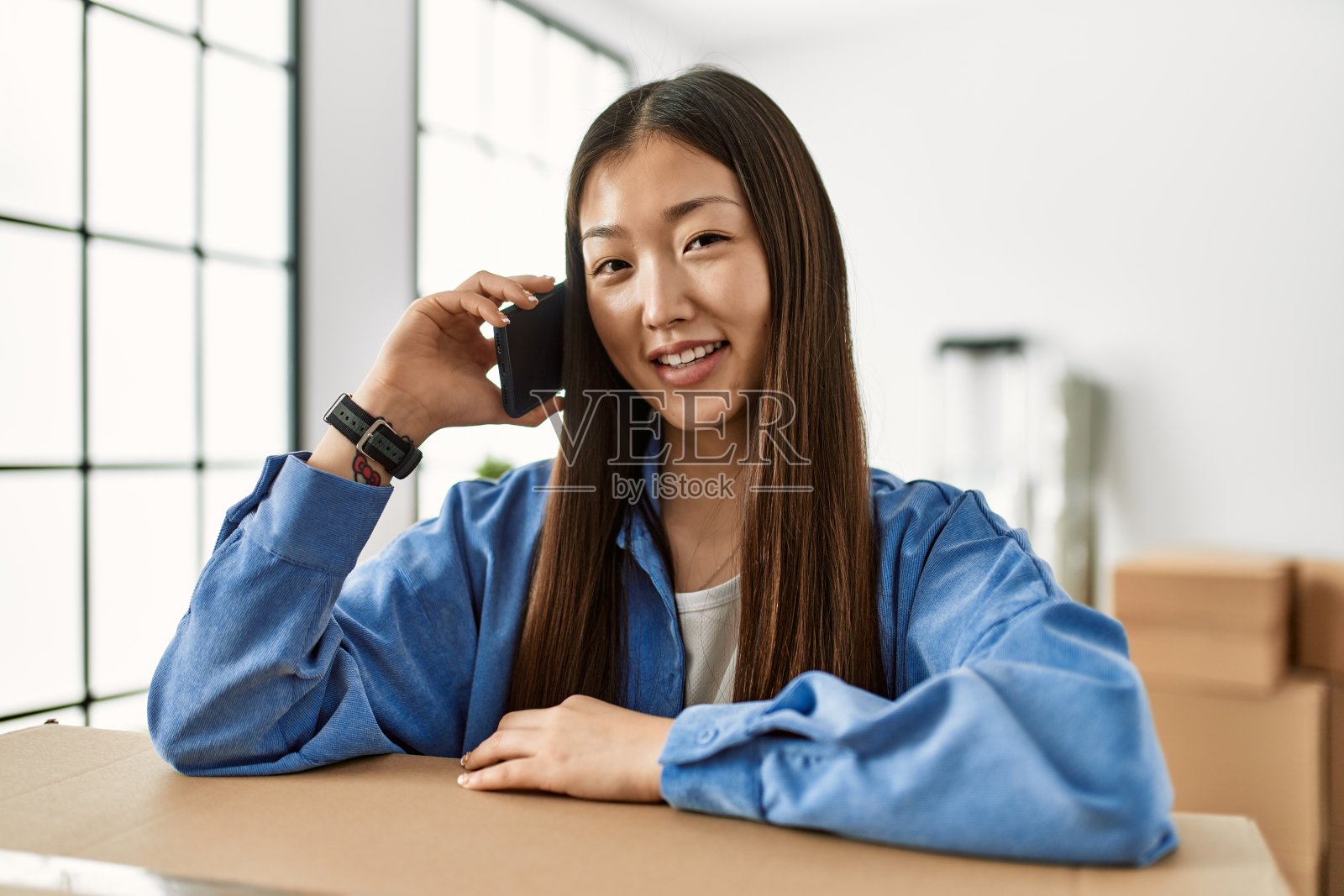 年轻的中国女孩微笑着在新家愉快地用智能手机聊天照片摄影图片