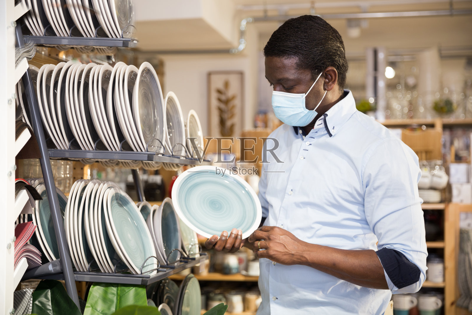 戴面具的非洲裔美国人在店里挑选餐具照片摄影图片