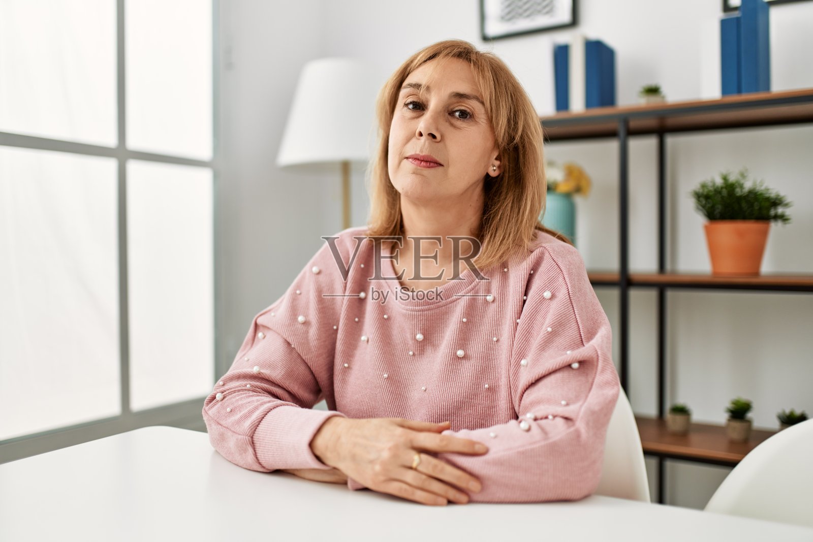 中年白人女性，穿着休闲装，坐在家里的桌子上，脸上带着严肃的表情。简单自然的看着相机。照片摄影图片
