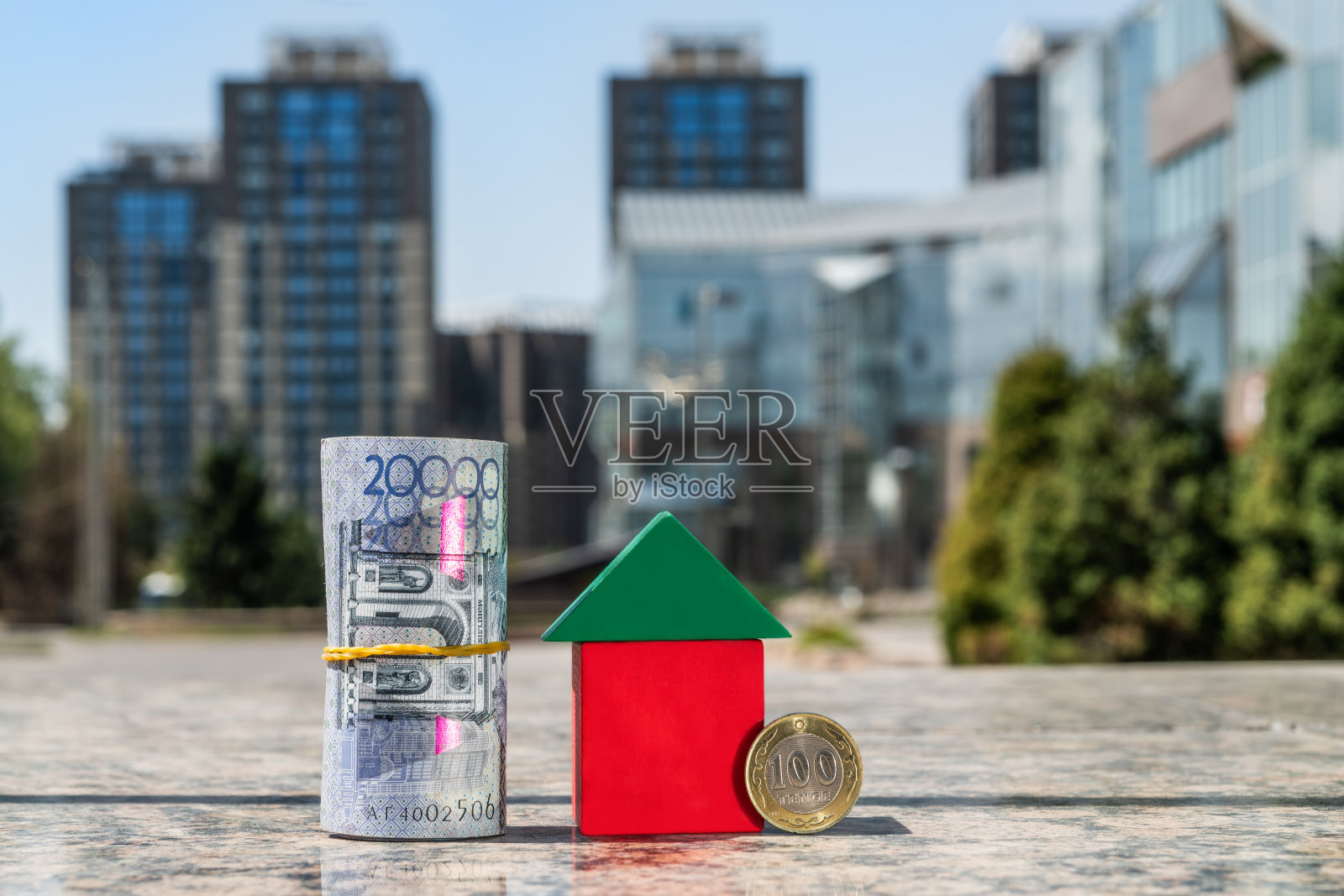 哈萨克斯坦2万坚戈纸币和100坚戈硬币在现代建筑背景下标志性的小房子旁边照片摄影图片