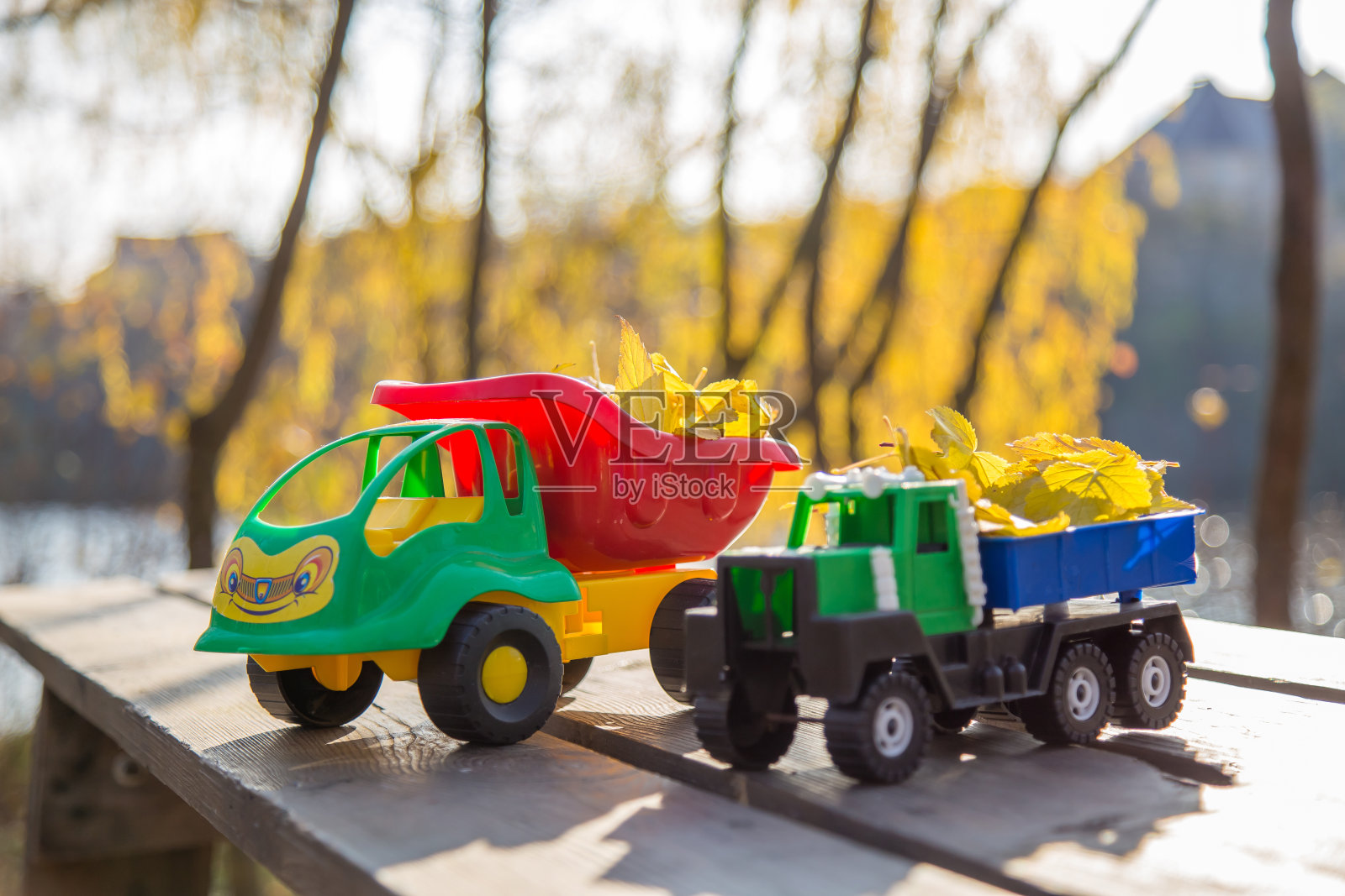 小玩具车停在木头表面，背景是一片模糊的秋天公园照片摄影图片