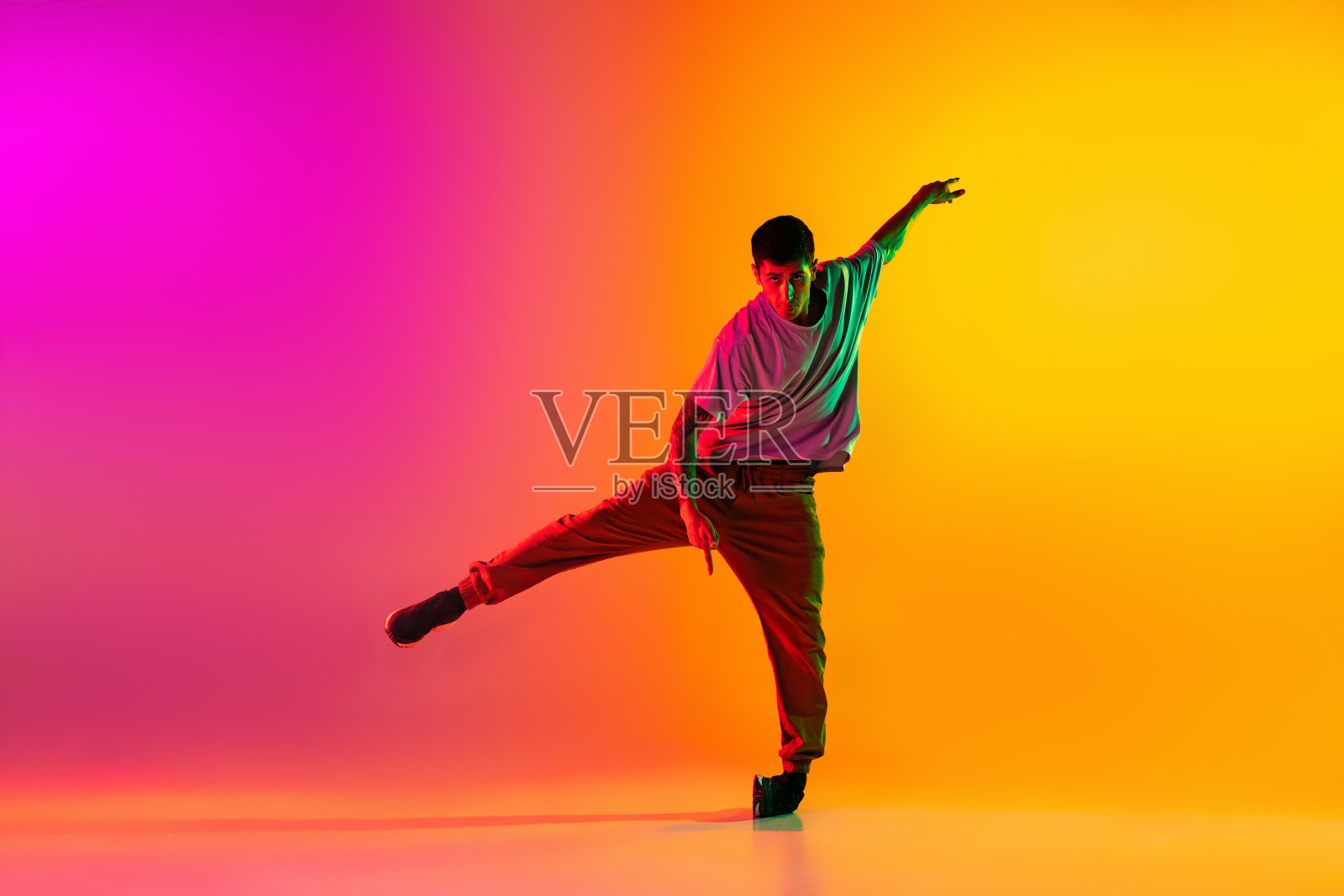 年轻时尚男人的肖像，霹雳舞舞者在霓虹灯下，在渐变的粉红色背景下孤立的休闲服装训练。照片摄影图片