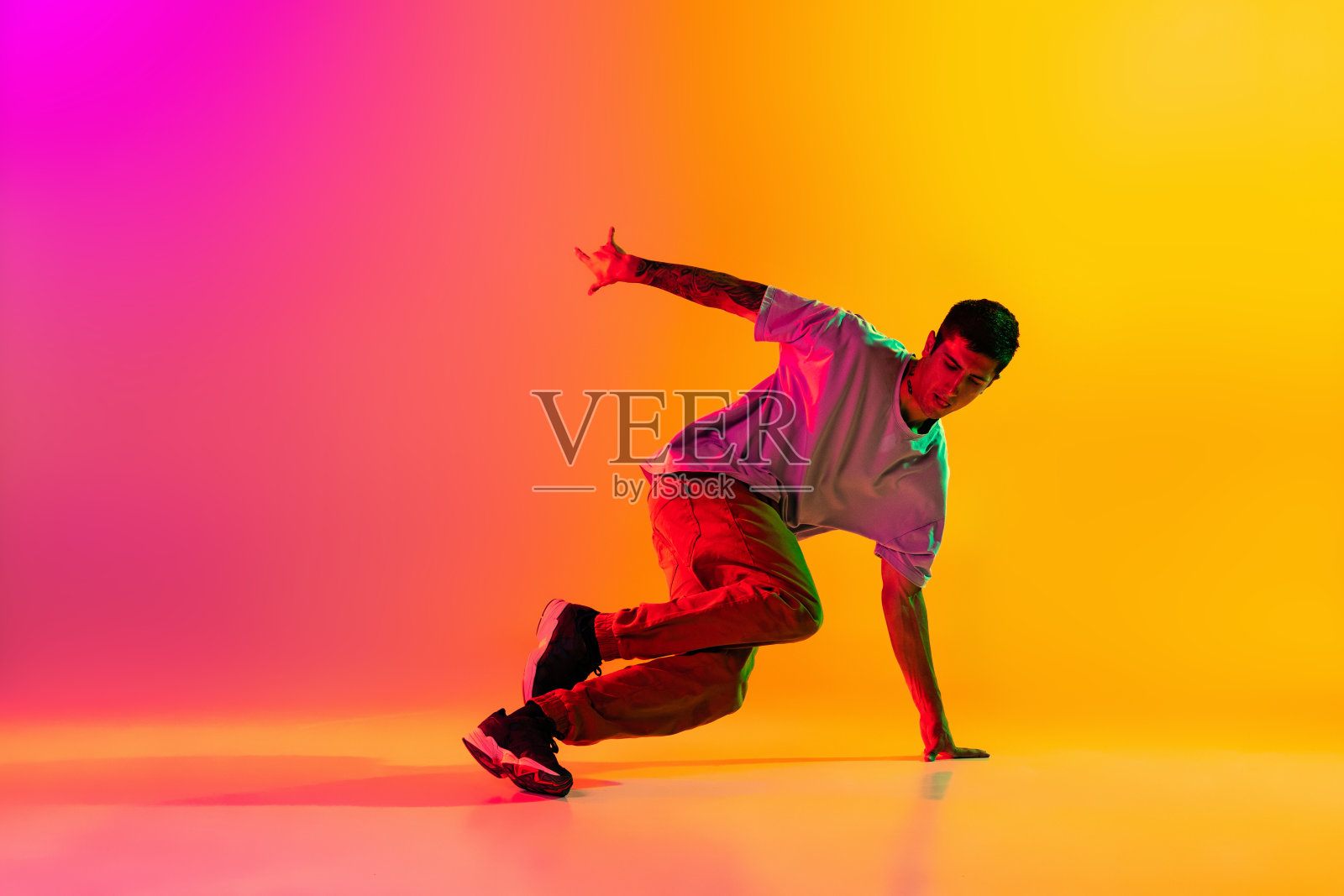 年轻时尚男人的肖像，霹雳舞舞者在霓虹灯下，在渐变的粉红色背景下孤立的休闲服装训练。照片摄影图片