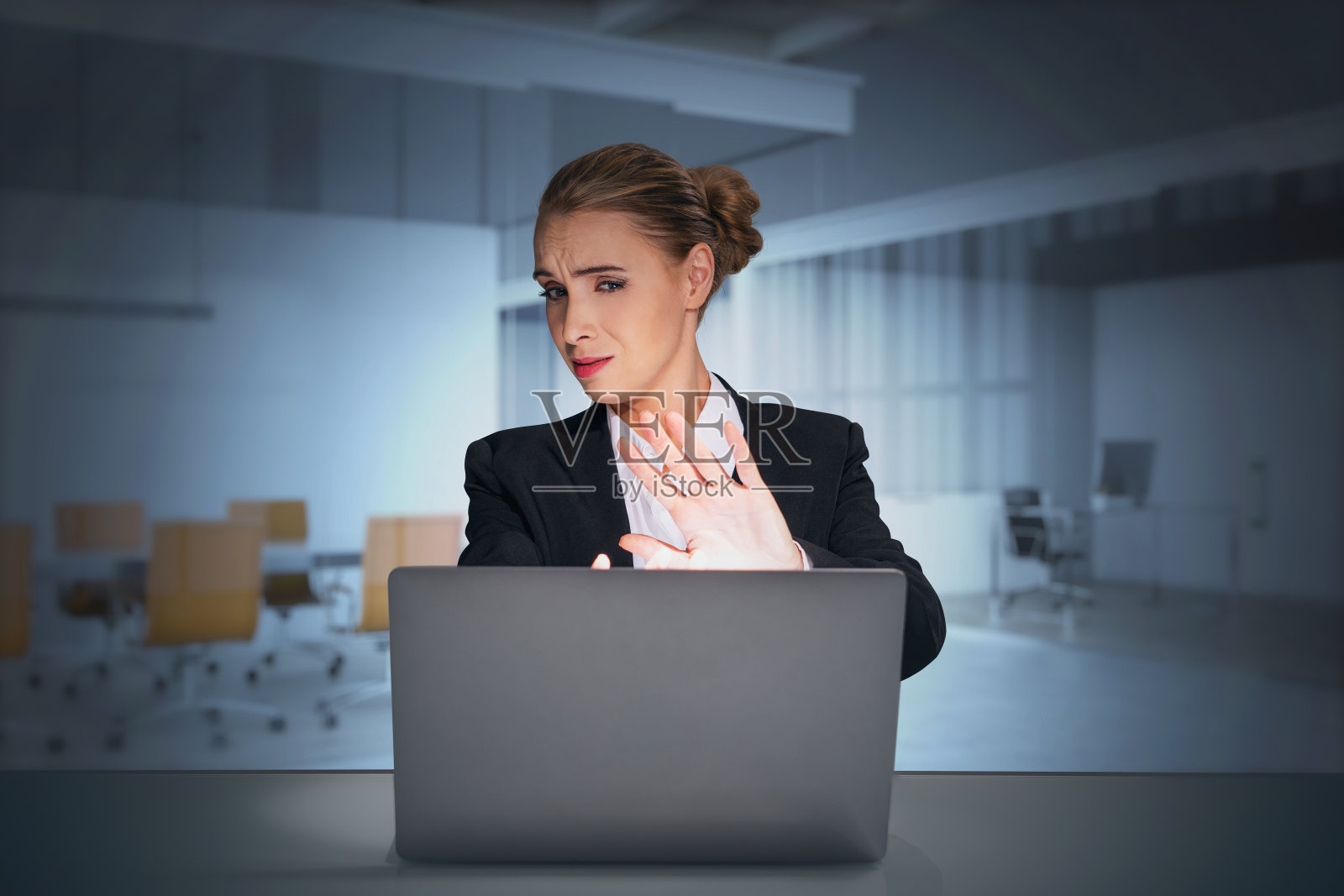 年轻的女企业家金融分析师穿着西装坐在办公室里，看着笔记本电脑屏幕，用手做出“停止”的手势，表示全球危机和负面新闻的概念照片摄影图片