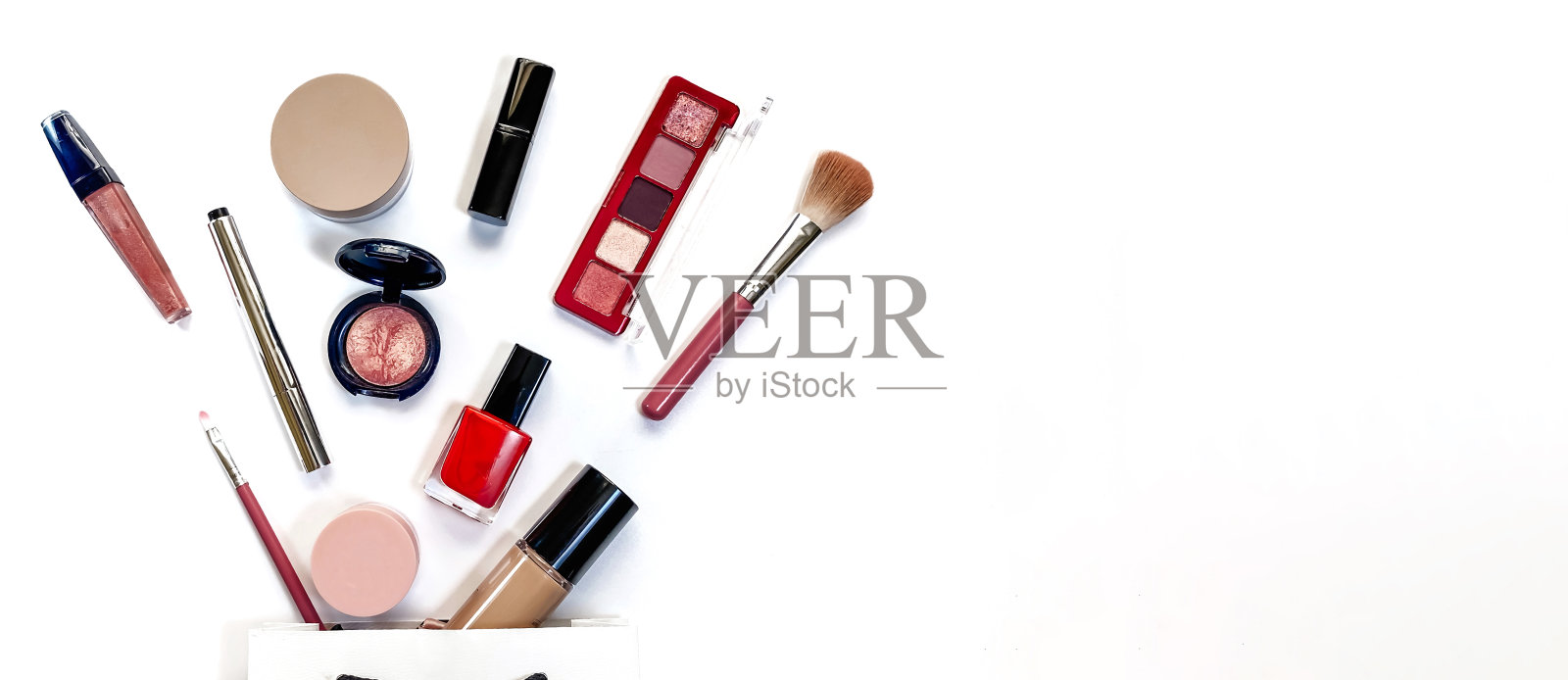 美丽的概念。化妆产品阴影，高光，腮红，刷子，粉，亮片，睫毛膏，光泽，口红，铅笔在白色背景下白色礼品袋照片摄影图片