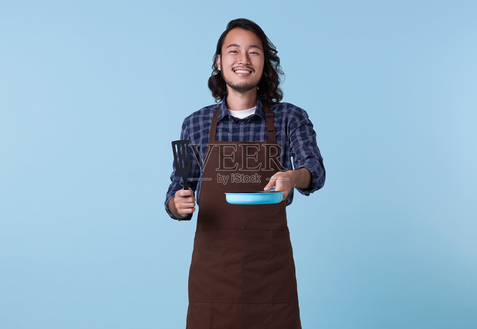 亚洲专业厨师准备烹饪，厨师拿着锅铲和煎锅孤立在蓝色背景上。照片摄影图片