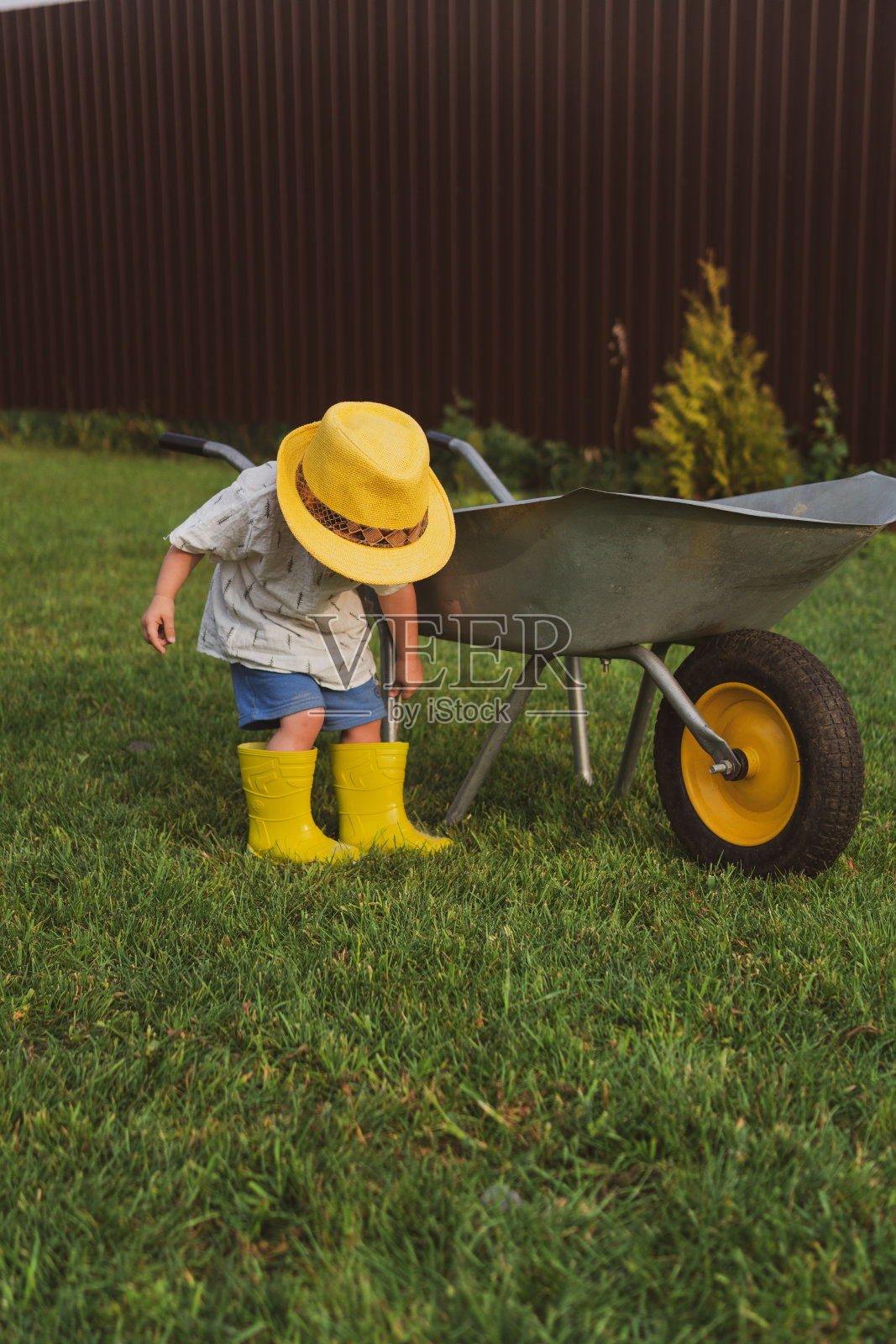 可爱的两岁小孩戴着草帽在装满沙子的花园手推车里玩耍照片摄影图片