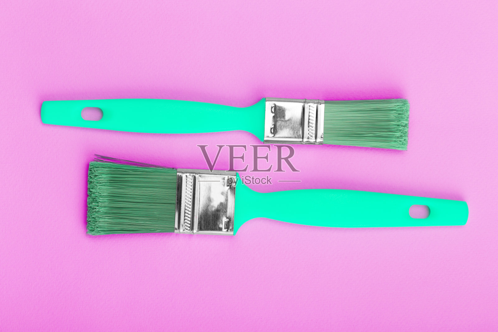 两支绿色的画笔在粉红色的纸纹理上作画照片摄影图片