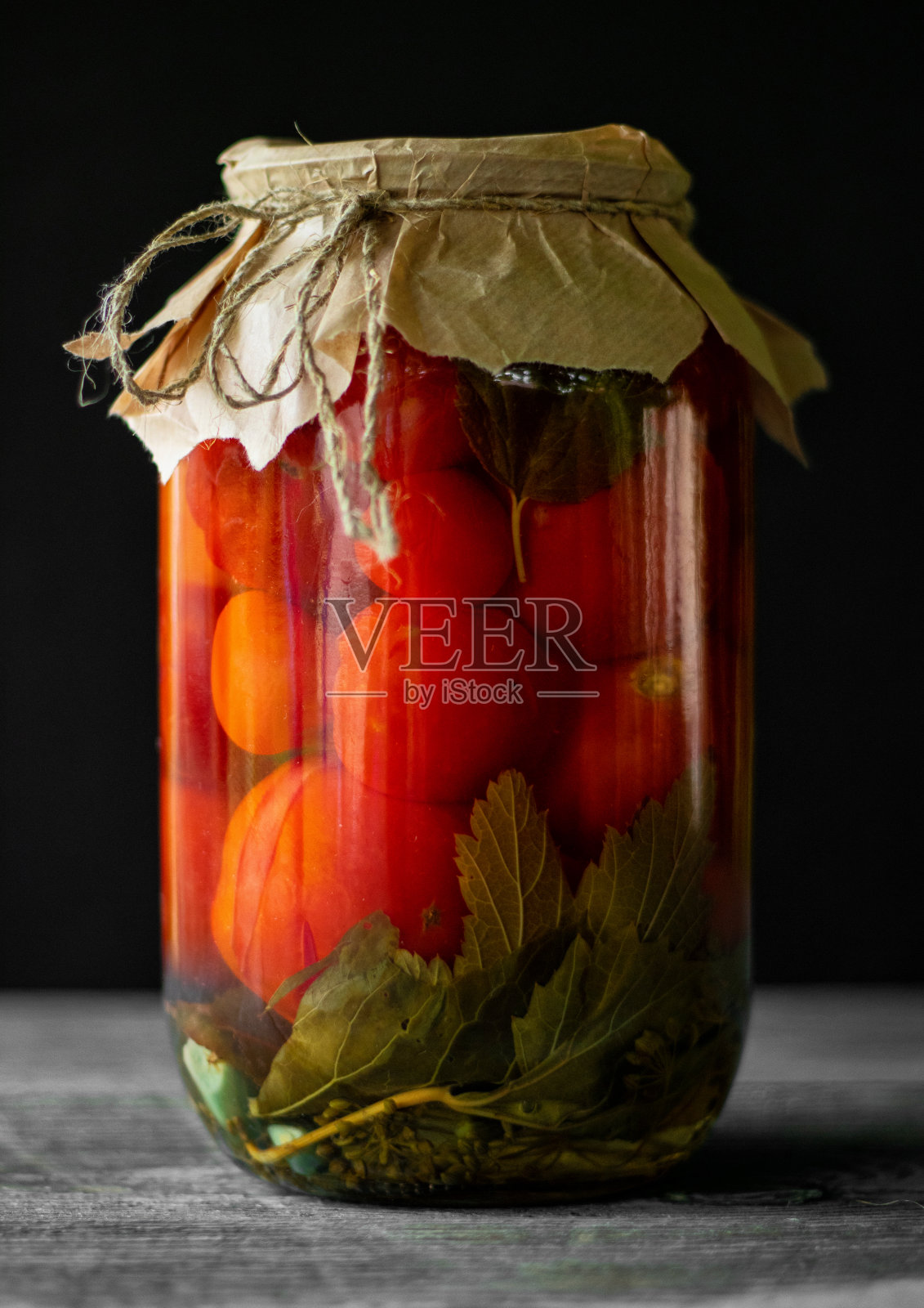 深色背景的旧木桌上放着一个玻璃罐里的腌西红柿照片摄影图片