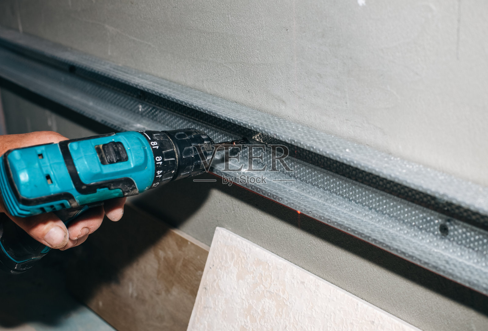 有人在灰色的混凝土上铺上白色的瓷砖。维修保养工程装修单位。恢复在室内。一个人正在用电钻工作。照片摄影图片