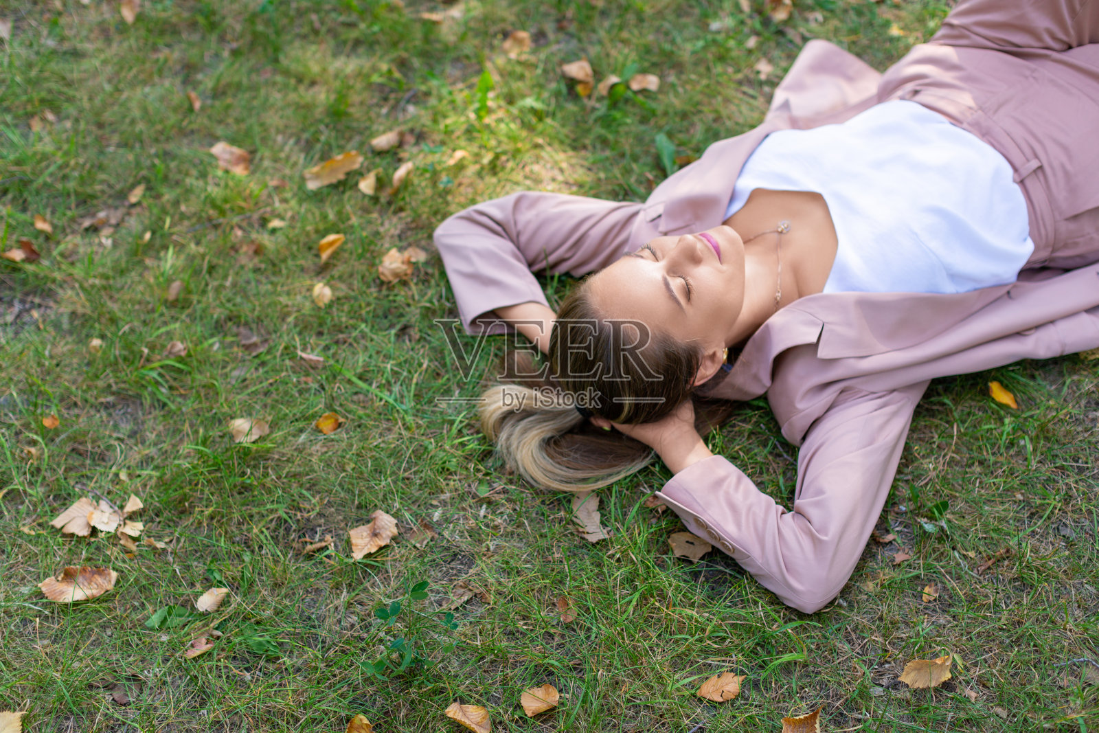 数码排毒概念——沉思的年轻女子闭着眼睛躺在公园的草地上。特写俯视图照片摄影图片