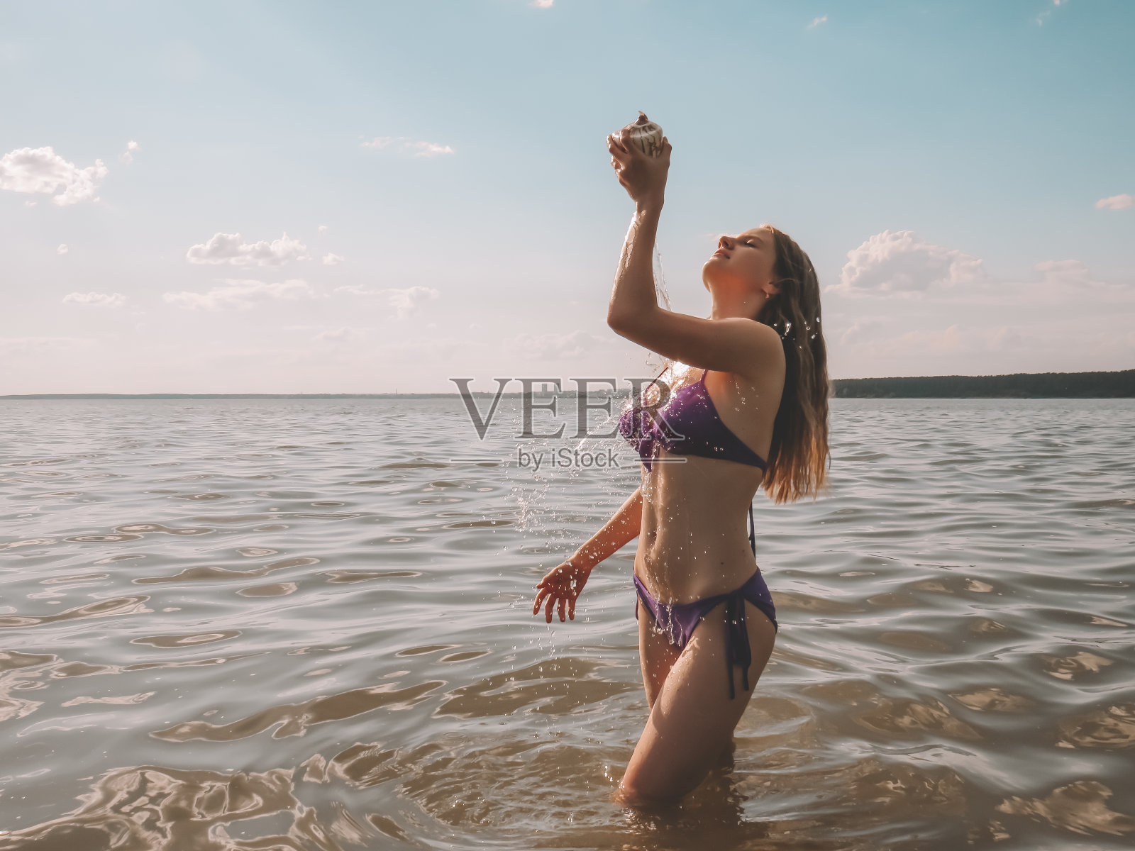 身穿比基尼、身材苗条的年轻女子从贝壳中倒水照片摄影图片