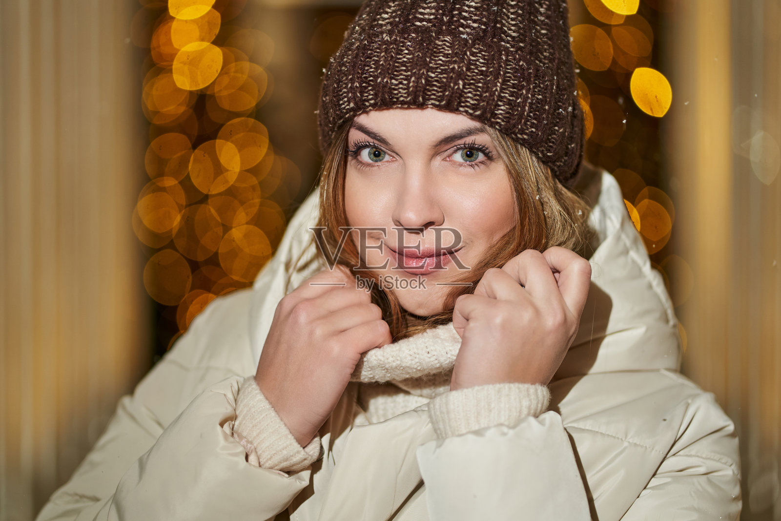 一个年轻美丽的女孩的特写肖像，穿着一件轻便的夹克，一顶棕色的帽子和一件高领毛衣。模糊的黄色灯光背景照片摄影图片