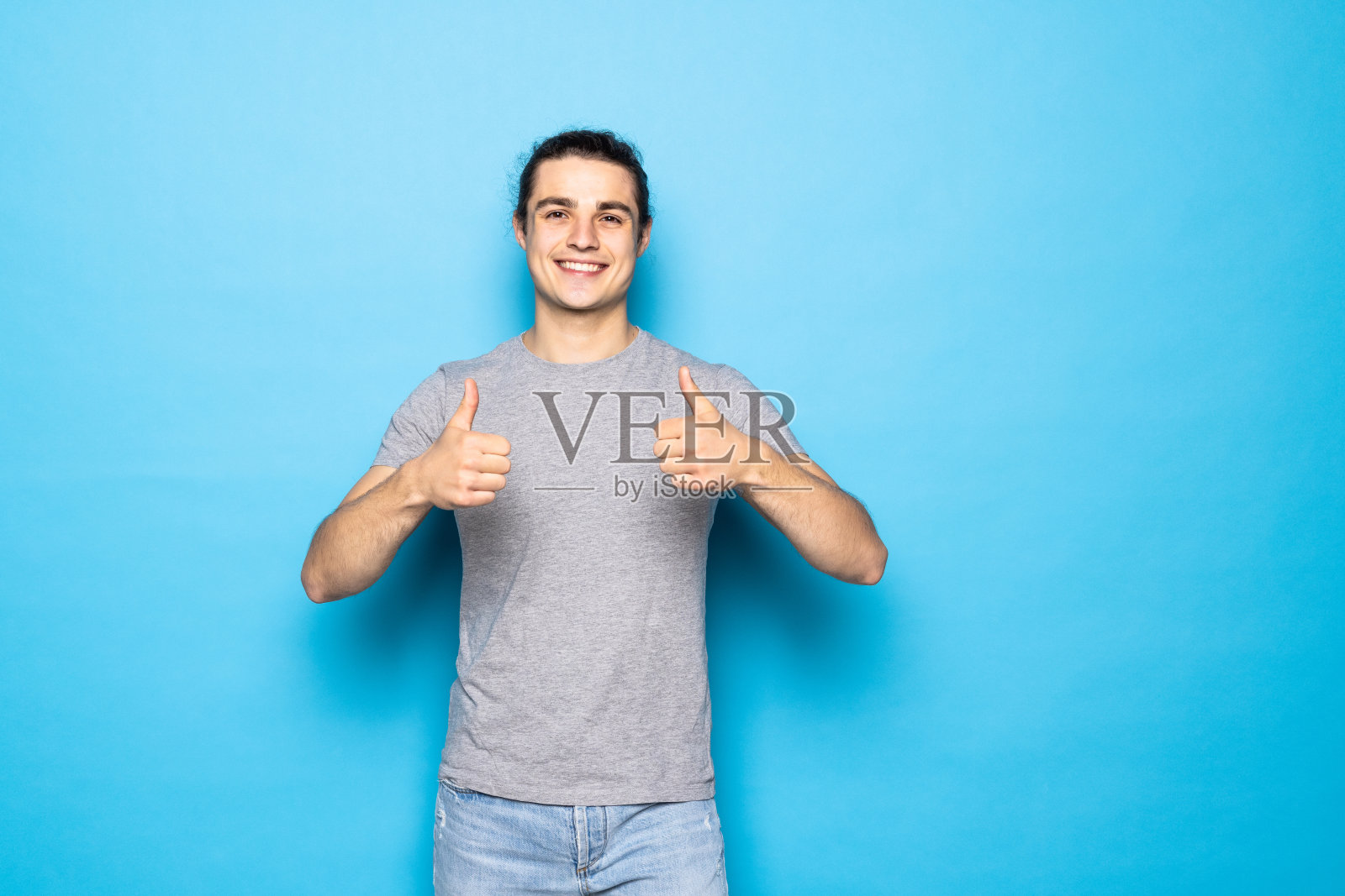 年轻英俊的男子越过蓝色背景成功手势做积极的手势与手，大拇指向上微笑和快乐。开朗的表情和胜利者照片摄影图片