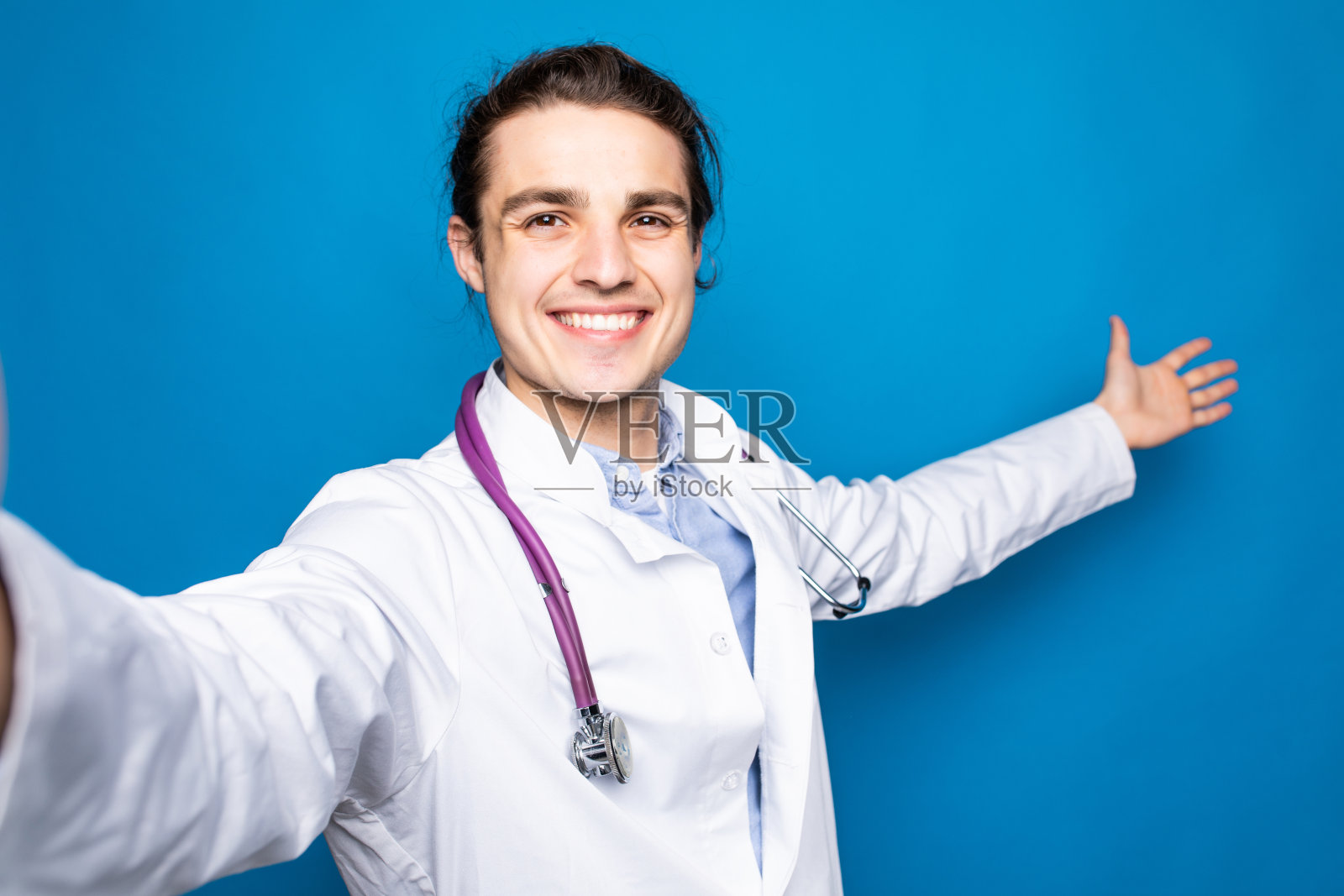 成年医生手持听诊器，独自站在蓝色背景下自拍照片摄影图片