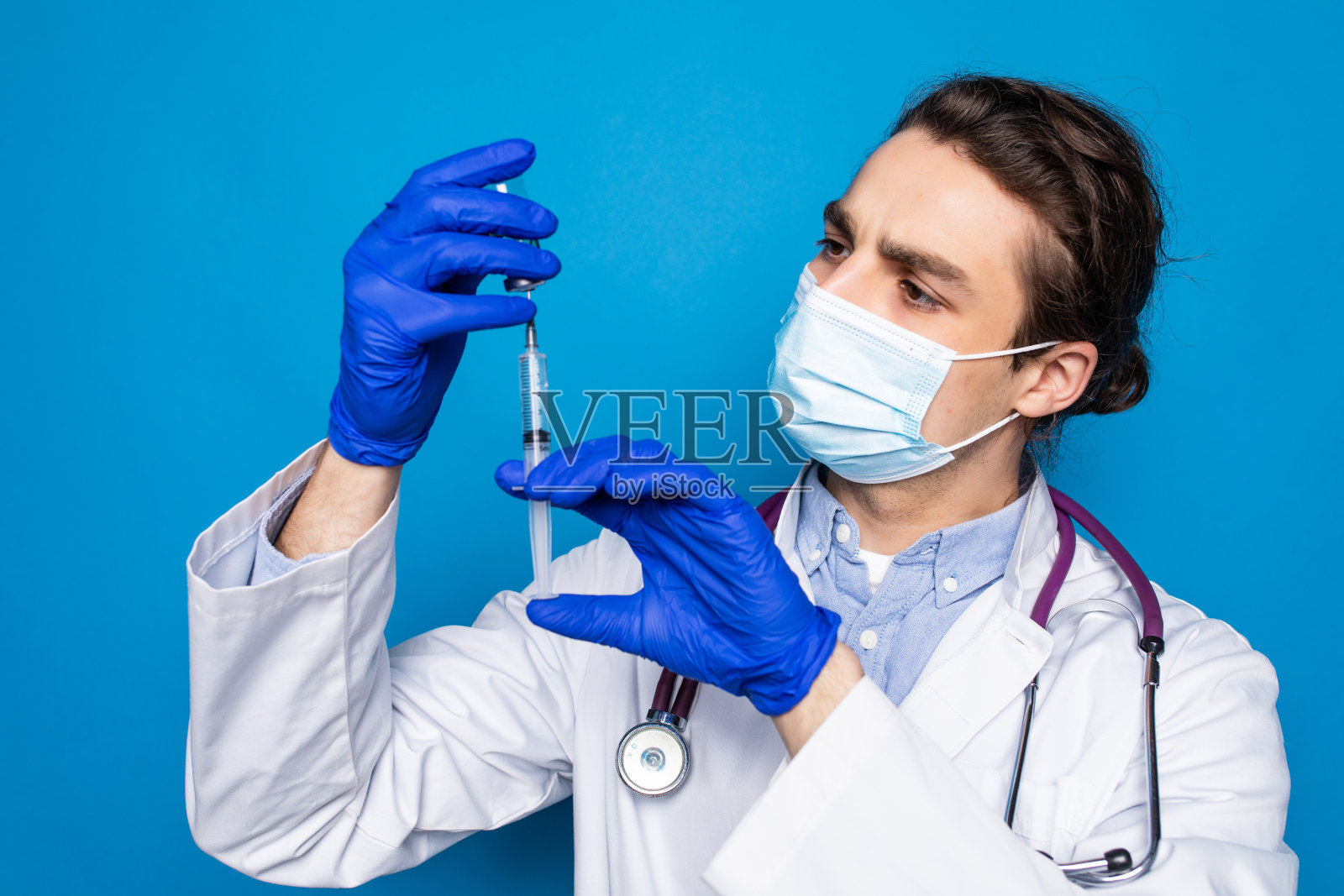 年轻的医生拿着注射器孤立在蓝色背景上。照片摄影图片