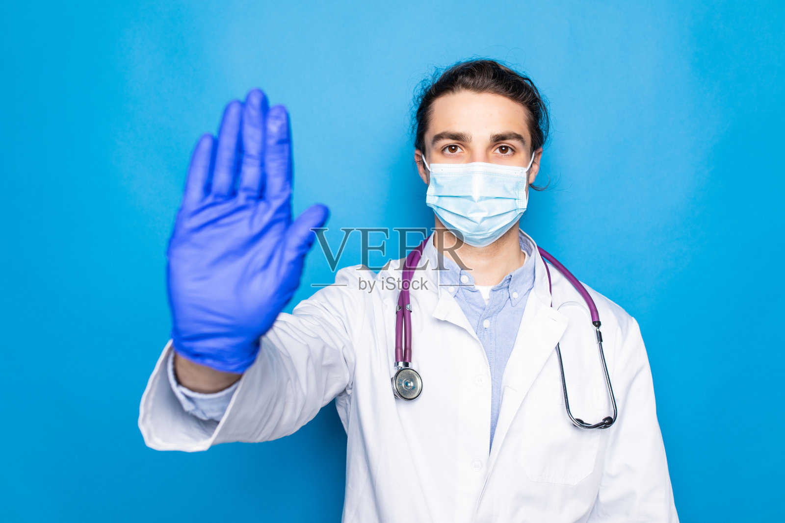 英俊的秃头医生，留着胡子，戴着眼镜和听诊器，在蓝色的背景下做着停止用手掌唱歌。照片摄影图片